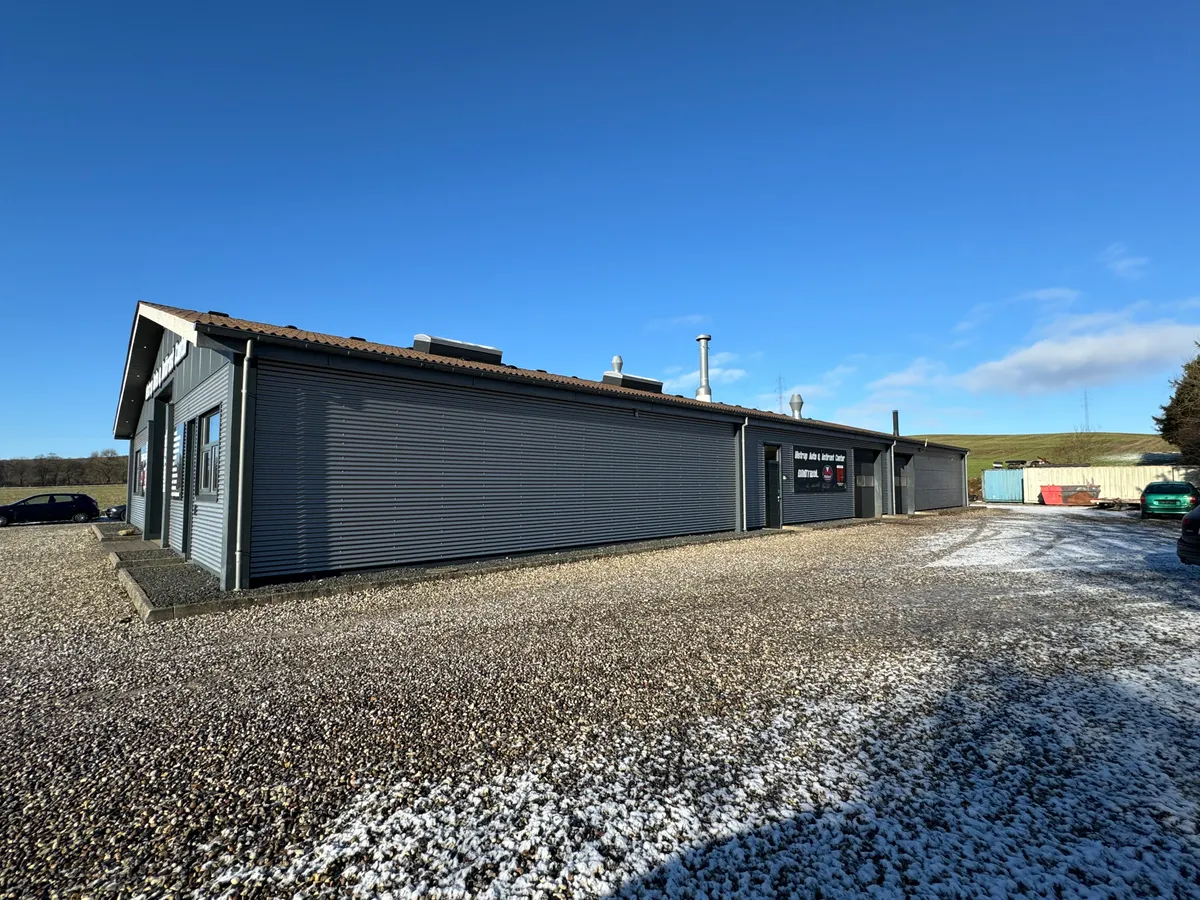 En stor, grå bygning med mange vinduer og skilte udenfor, der er placeret på en jorddæmning med sne og sten.