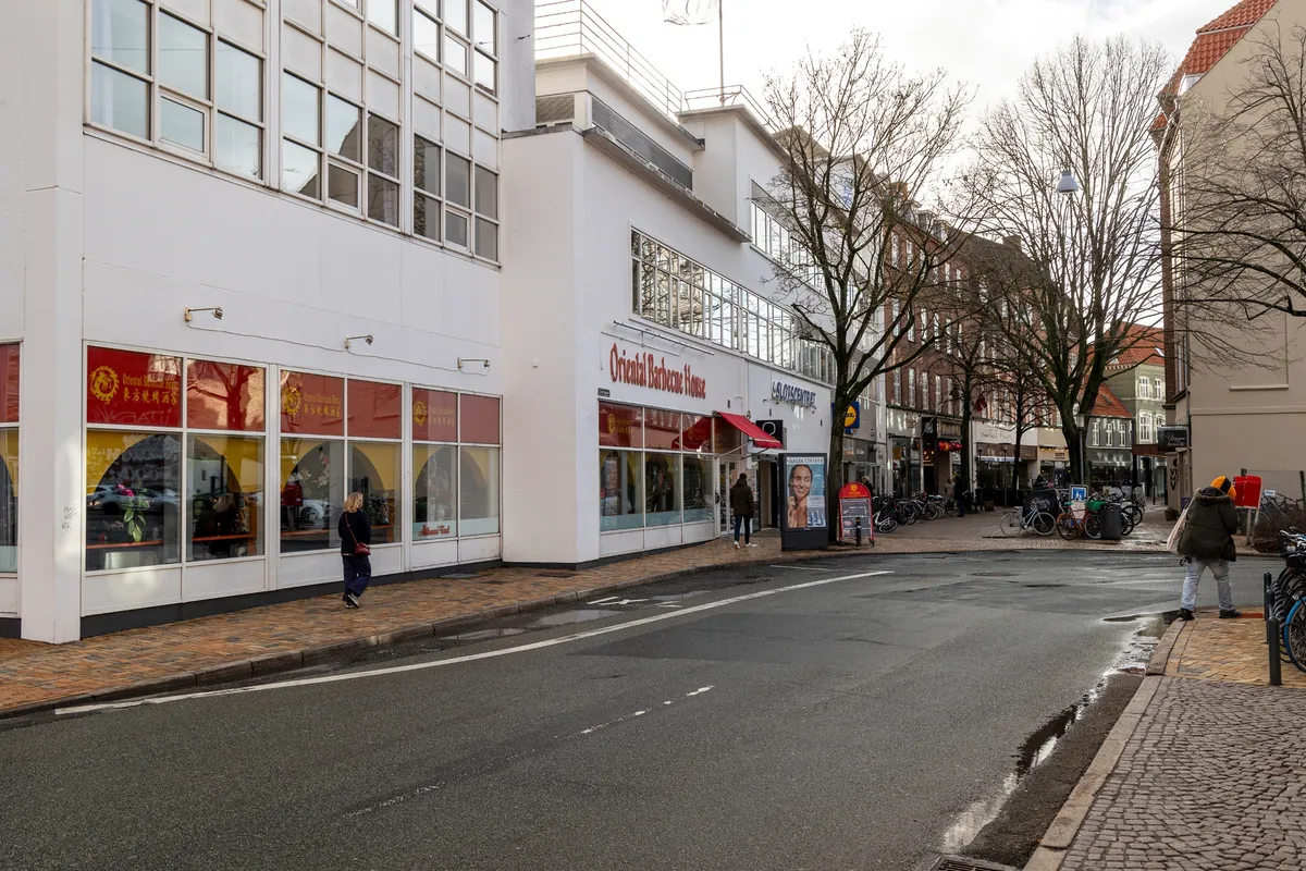 Mennesker går på gågaden foran ejendomskomplekset Slotscentret i Odense, og der er flere cykler parkeret langs siden