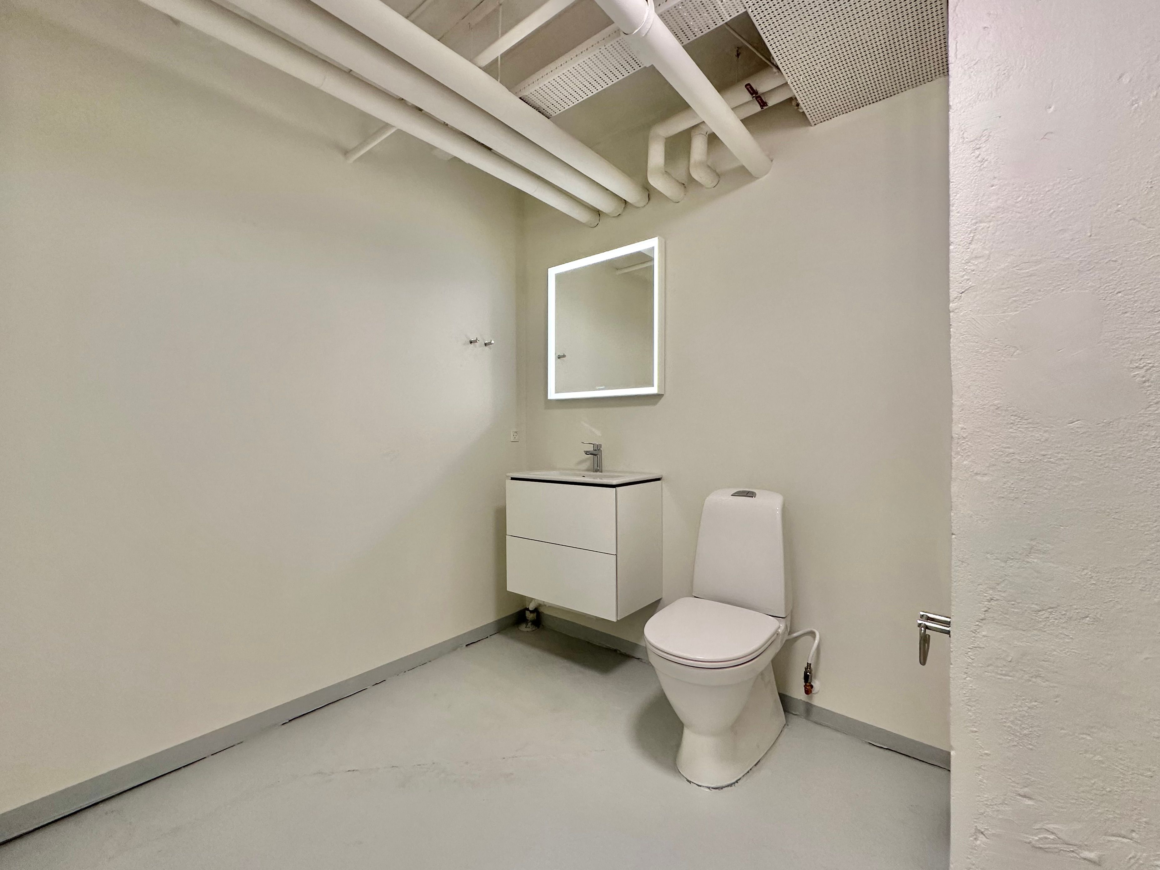 Et lille toiletrum med en hvid toilet, en hvid vaskeskab og en hvid spejl med en lysekrans.