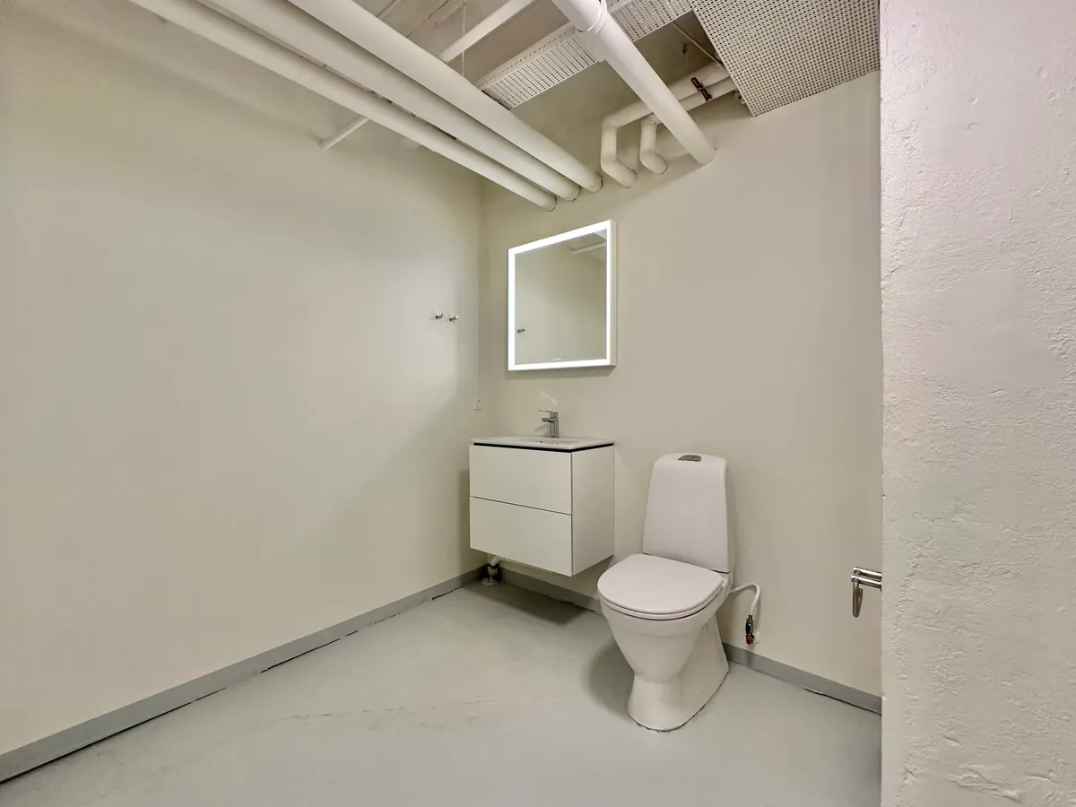 Et lille toiletrum med en hvid toilet, en hvid vaskeskab og en hvid spejl med en lysekrans.