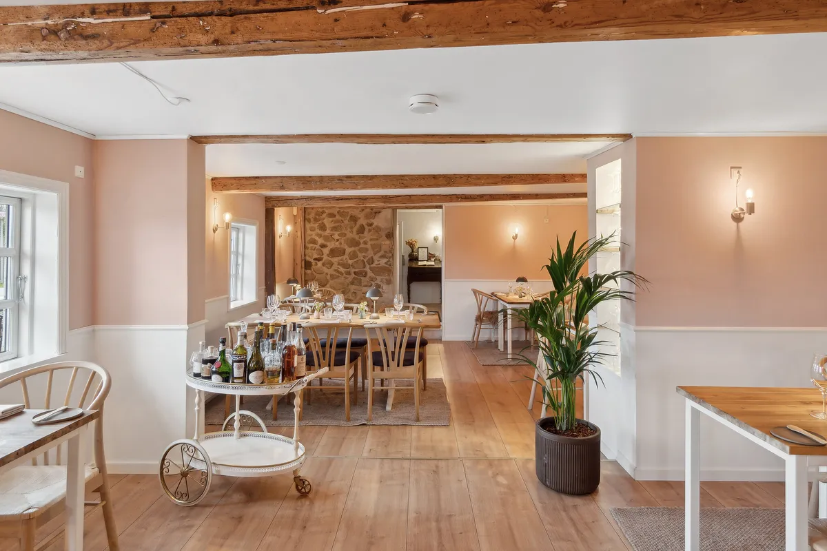 En indretning med en lang træbænk, flere træborde og stole samt en plante i en brun potte