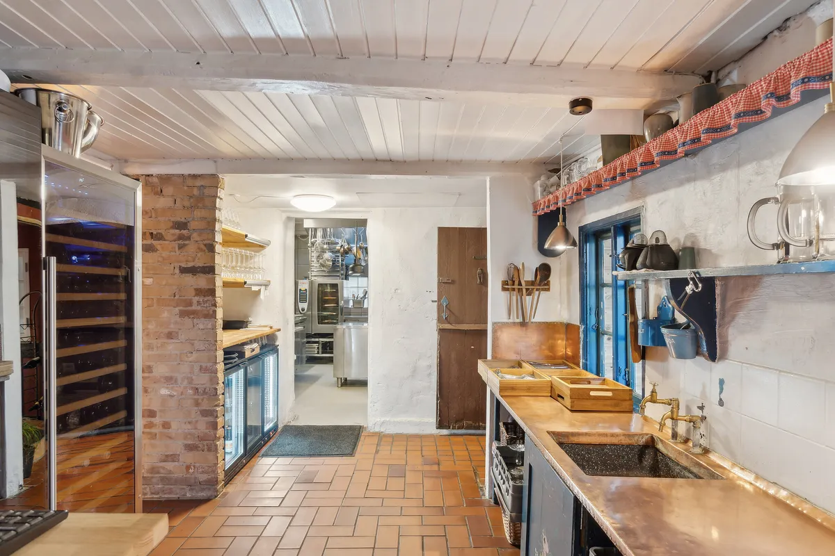 Et køkken med lyse loftsbjælker, kobber vasketøj, køkkenudstyr og trægulve og en søjle med røde mursten