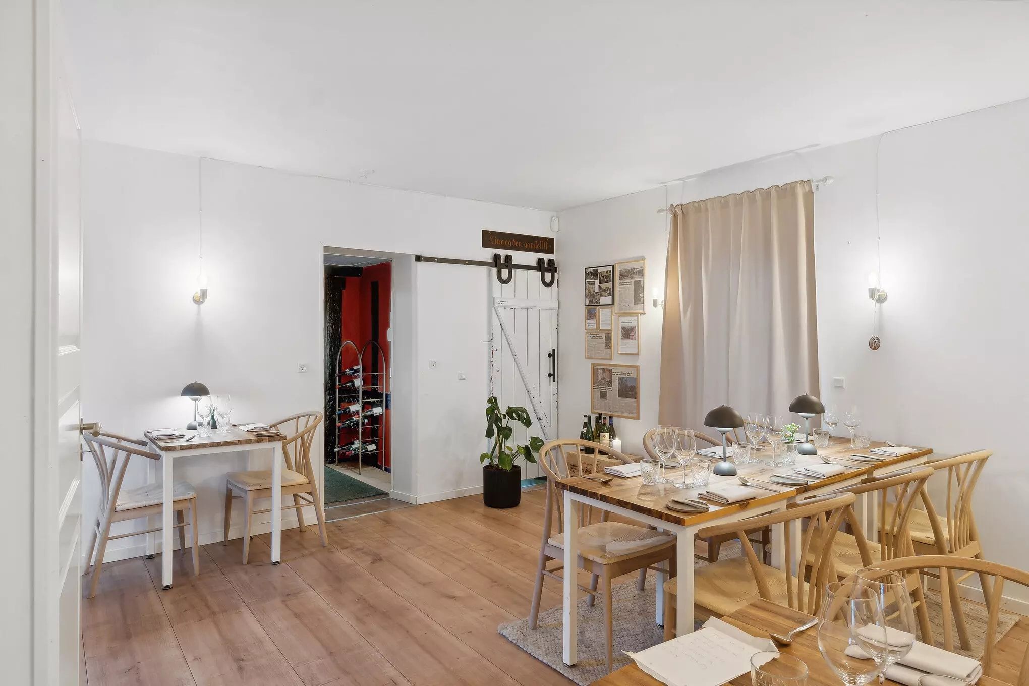 Moderne restaurant med to spisesteder, hvor et bord er dækket og det andet har stole med høje ryggelæn og vinglasser