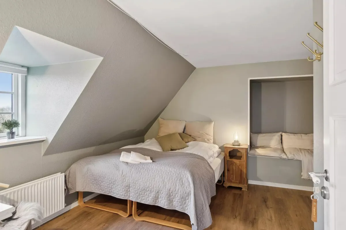 Et soveværelse med et enkelt seng og to hovedpuder, et lille bord med en lampe og et træskab