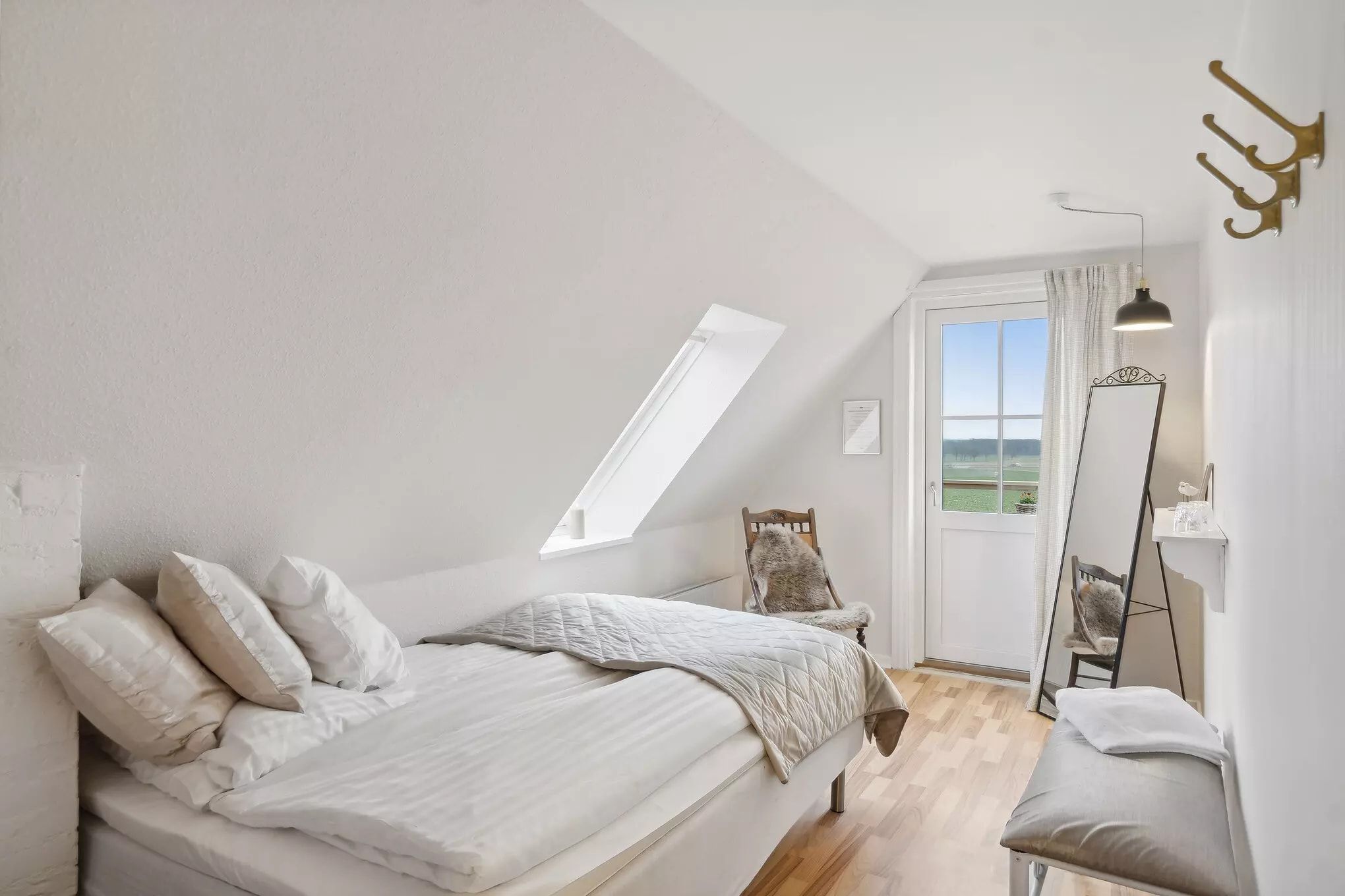 Søvnværelse med hvidt loft, hvide vægge, et dobbeltseng med tæt lag af tæpper og puder og et tøjstativ med hængende lamper