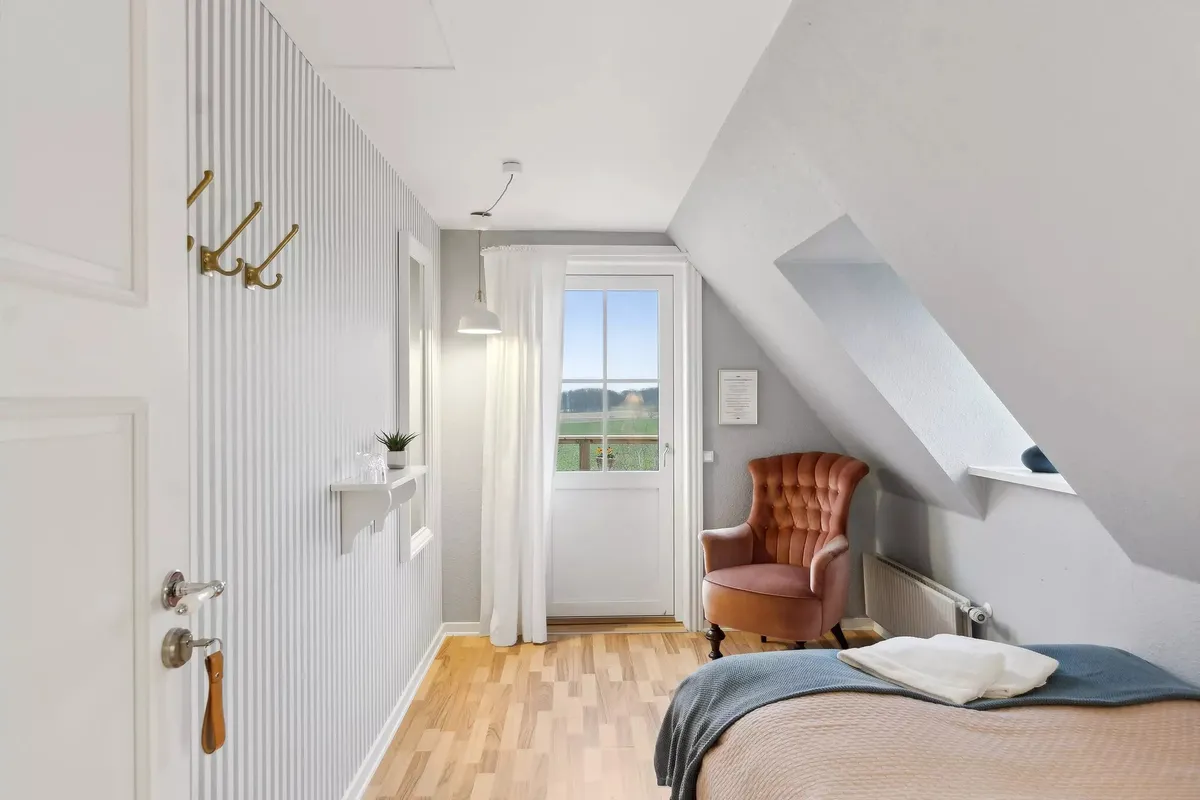 Soveværelse med højloft, hvidt loft, lysegardin, lysekronen, to træklatre og en trægulv.