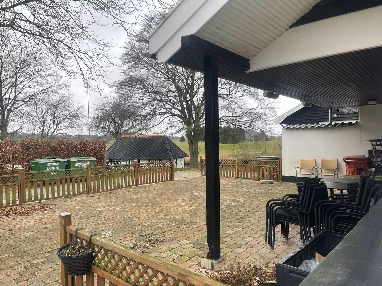 En have med bord og stole, en køkkenhave og en gårdhave med en lille hytte i baggrunden