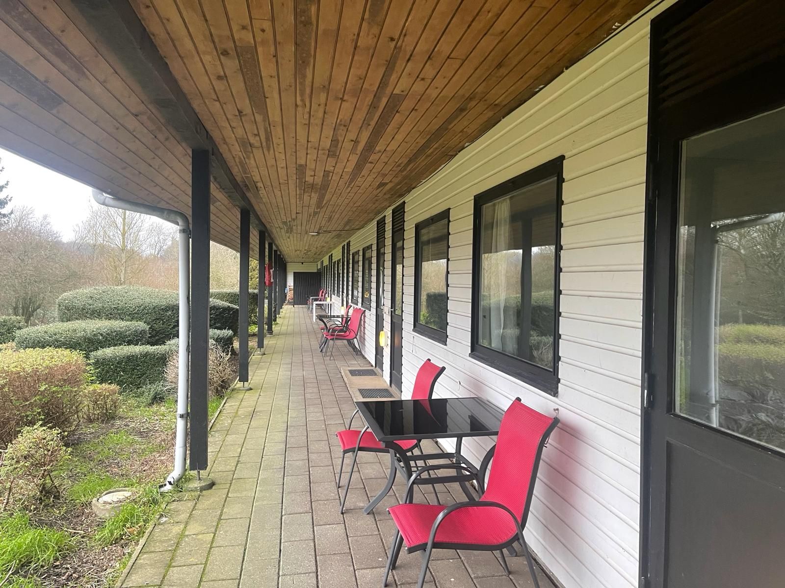 Lang veranda med røde stole og bord på terrassen med smuk udsigt over naturen