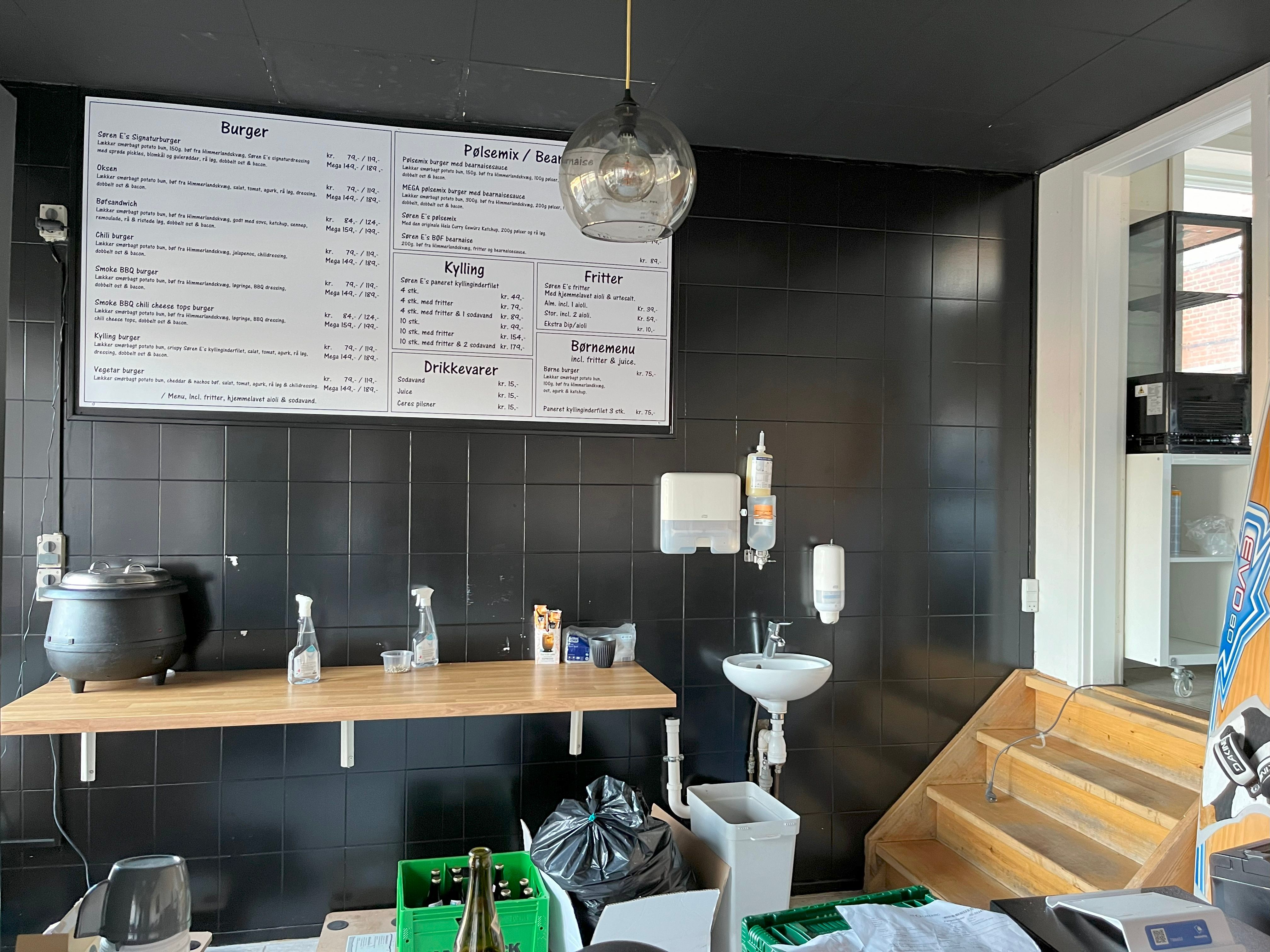 Burger menu med produkter som Lakker mearbørger og Kyllingeburger. Tilbehør som Fritter og Drikkevarer. Udstillet i en