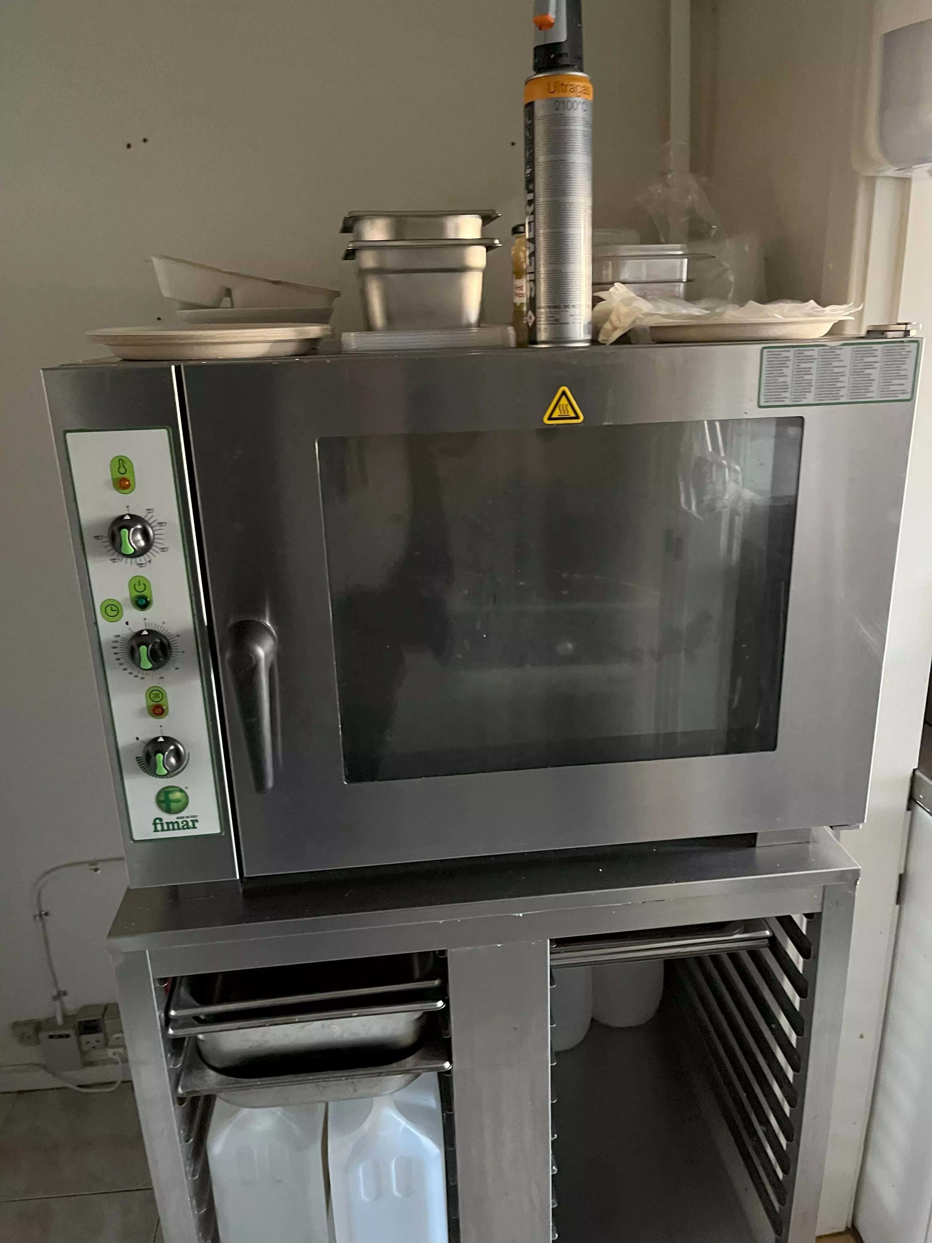 Fimar komfuret står på et metalbord med to plastflasker og to metalbakker med håndtag. Komfuret er lukket og har en stribet