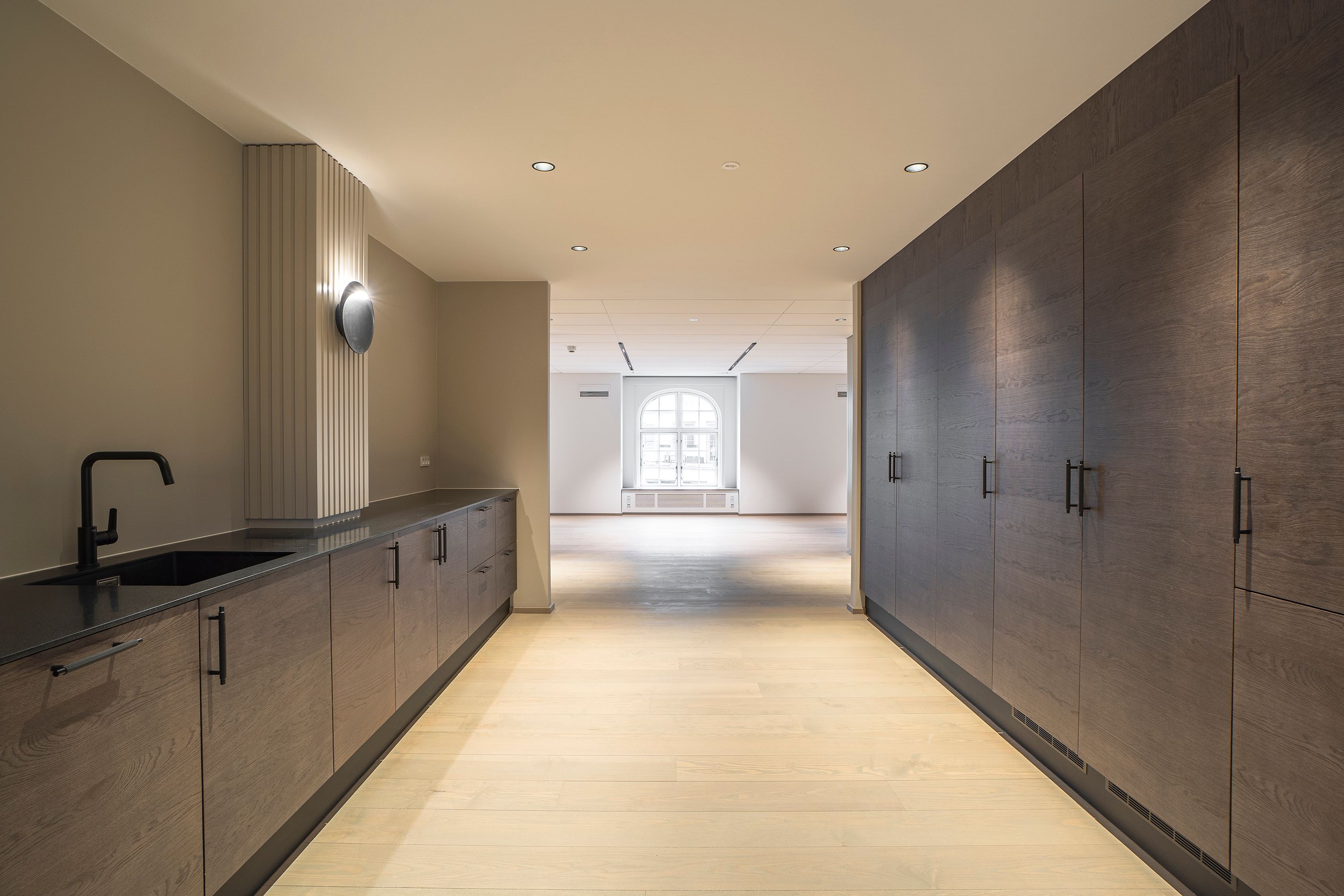 Moderne køkken med lyse træhylder og gult gulv. Sort vandhane med lys over skabet. Minimalistisk og funktionel design.