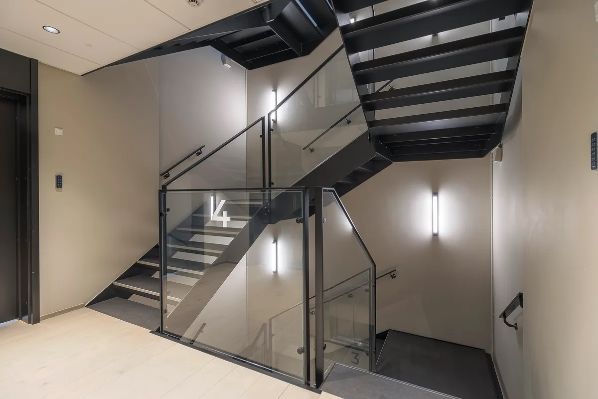 En moderne trappe med glasvægge og sort metal stiger op til et kontorlokal med nummeret 4. Styret i sort metal og gulvet med