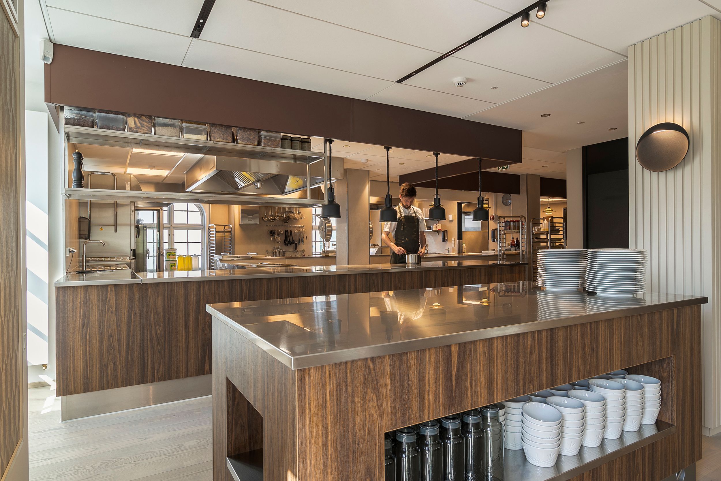 Moderne kommercielt køkken med rustfrit stål og træ. Væggen er dekoreret med mønstret. Køkkenbordene er udstyret med glas og