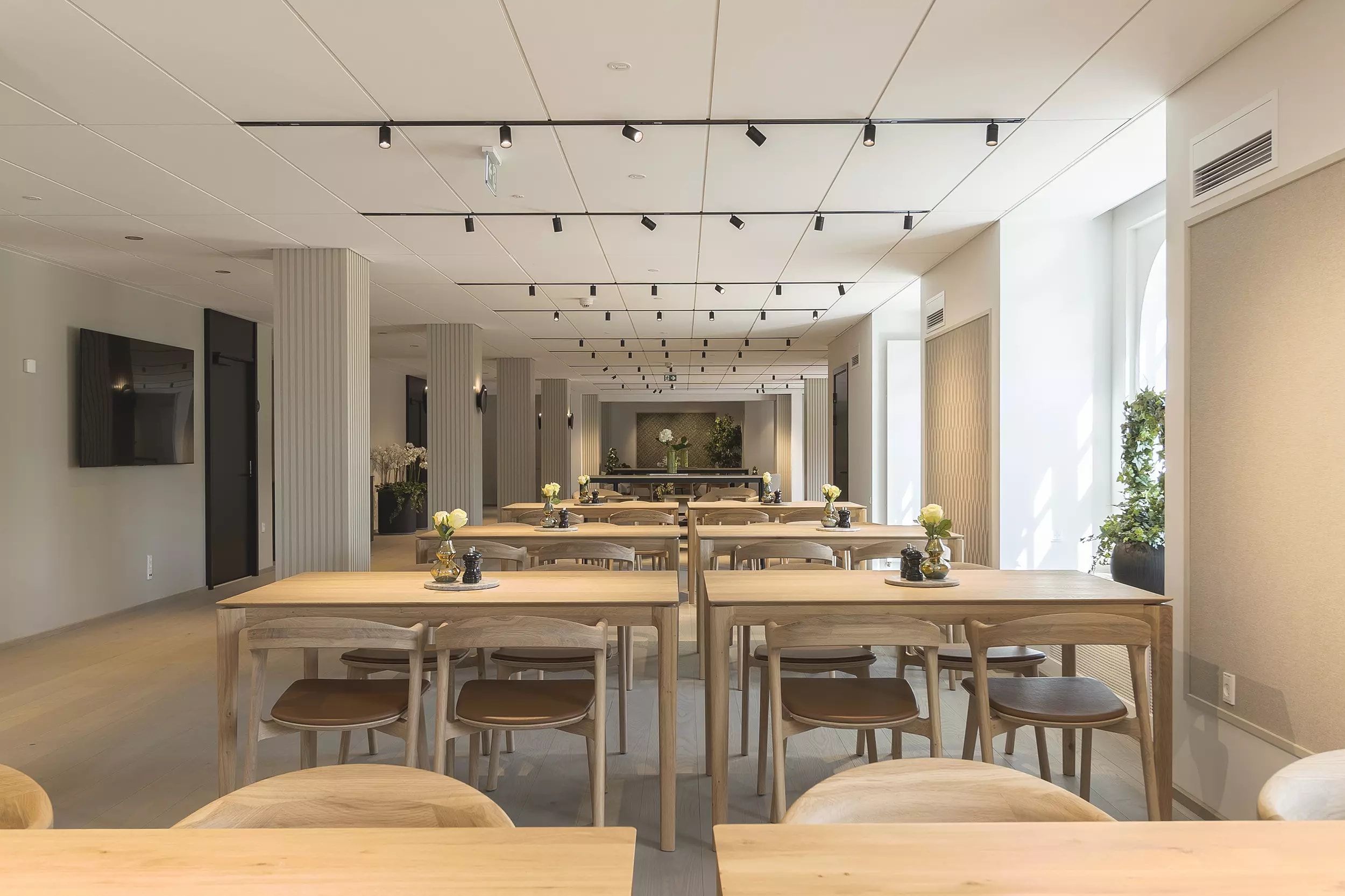 Lyst og elegant kontor med lyse vægge, træborde og stole samt kunstige planter og lysekroner i loftet