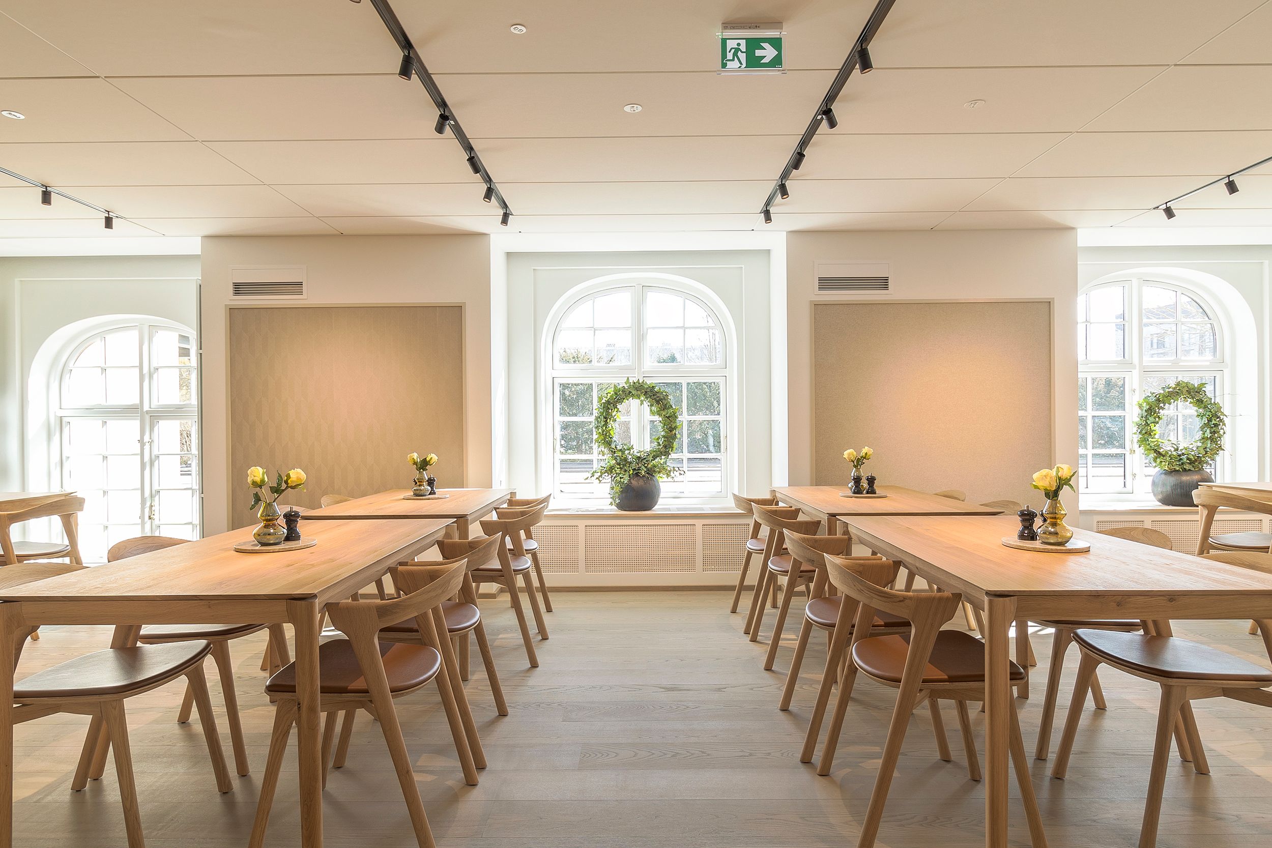 En flot mødehal med lyse træborde, stole og vinduerne med plantekranse i potteplanter
