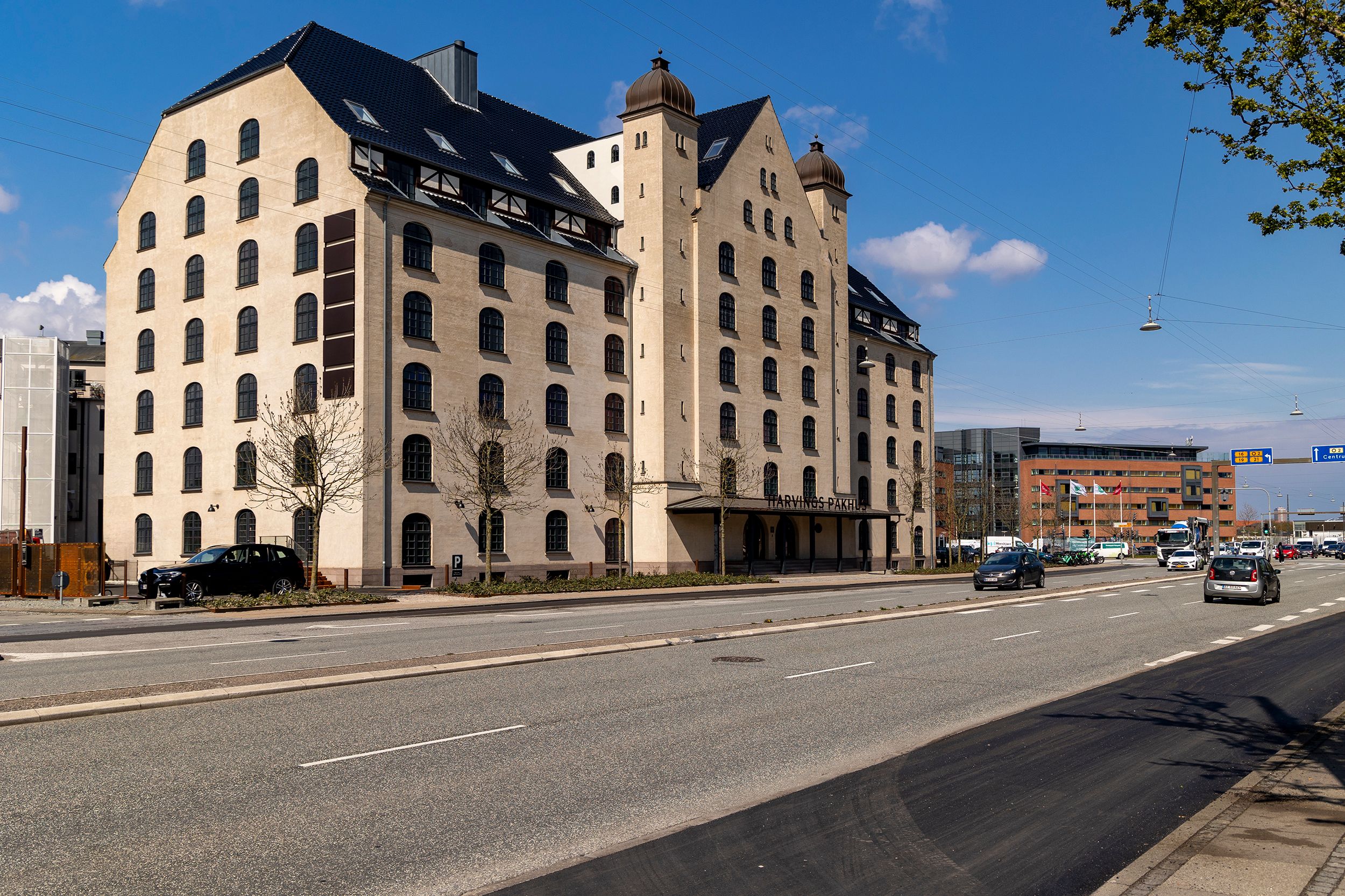 En stor bygning med mange vinduer og to kuppelformede tårne på gaden med biler og trær