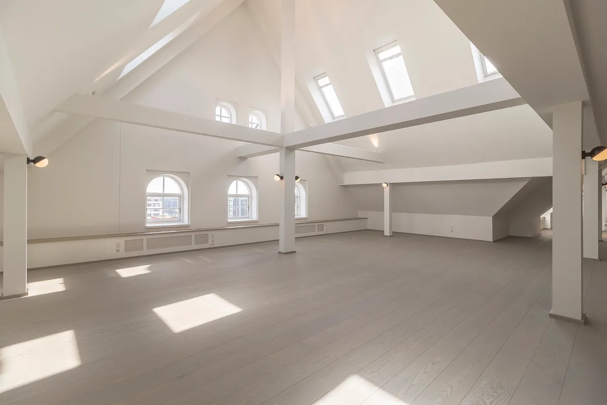 Et stort loft med højt til loftet, hvidt gulv og loftsvindue, der giver masser af lys til rummet