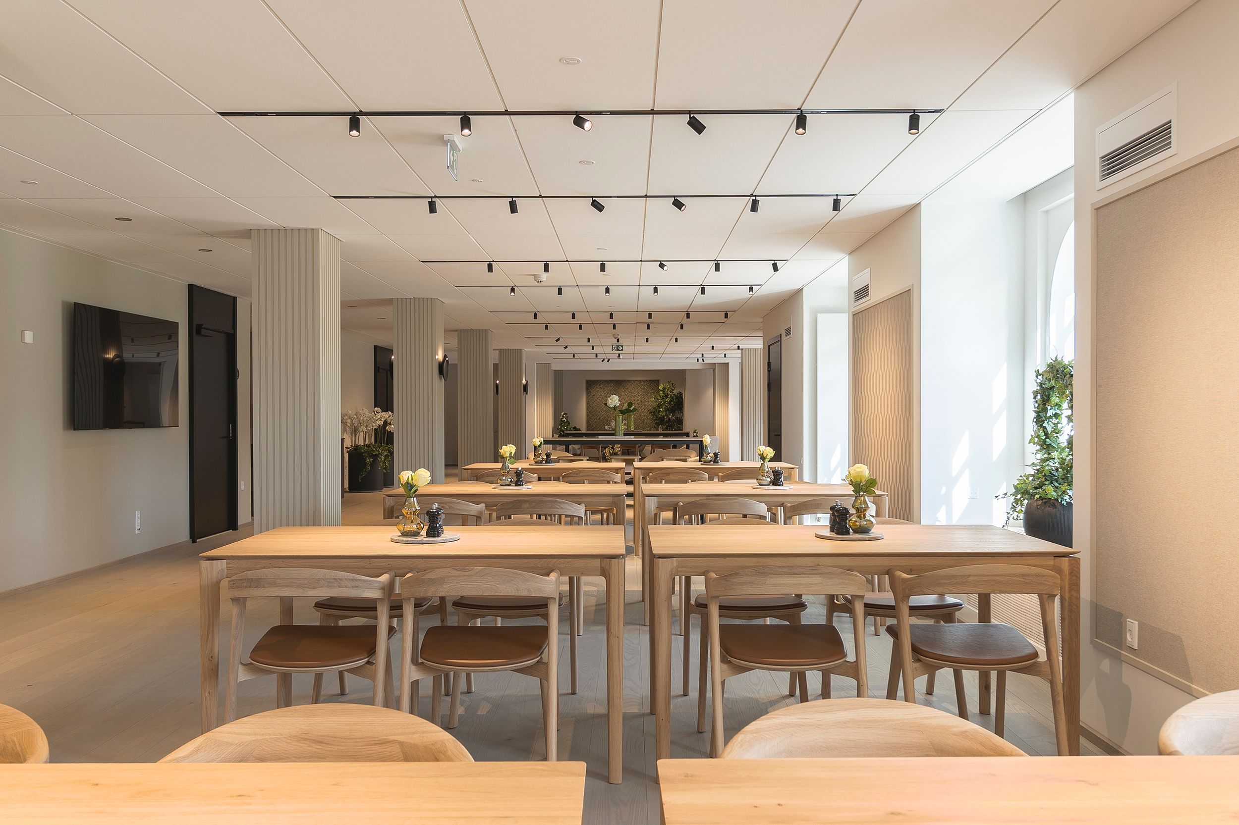 Indvendigt billede af en moderne konferencesal med lyse og rene møbler, lysekroner og store vinduer