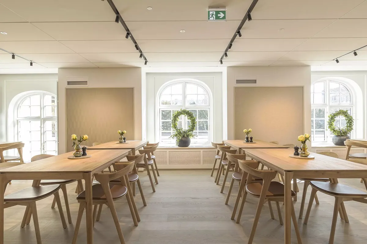 Lyst og moderne kantede møbler med lyse bænke og store vinduer. Dekorative lysekrans og plante i lyse farver.