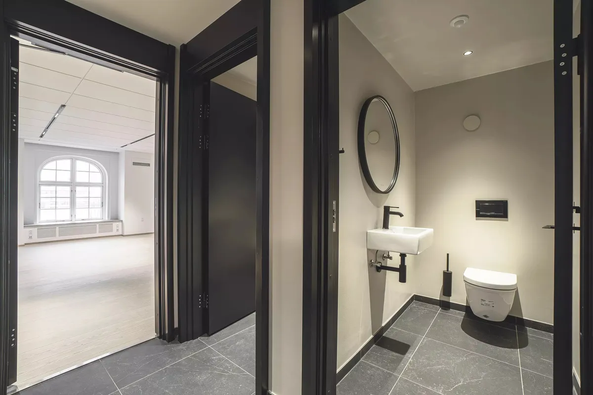 Toilet med sort dør og spejl. Toilettet er lukket og har en hvid keramik. Toiletbøsset er hængende og har en spidset