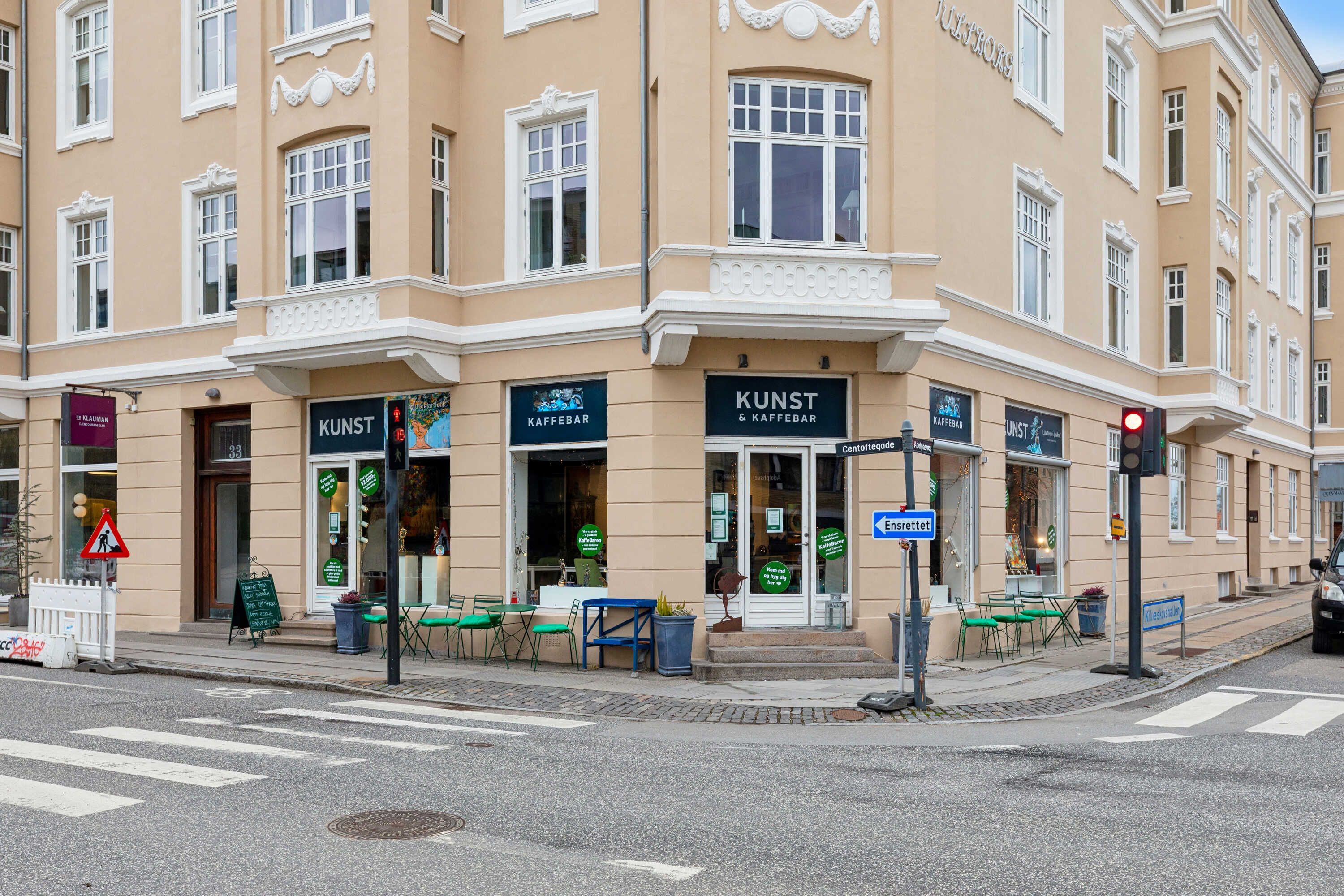 En gårdplads med tre caféer og et hjørne med kunstgalleriet Kunst & Kaffebar. Der er grønne stole og borde udenfor, og der