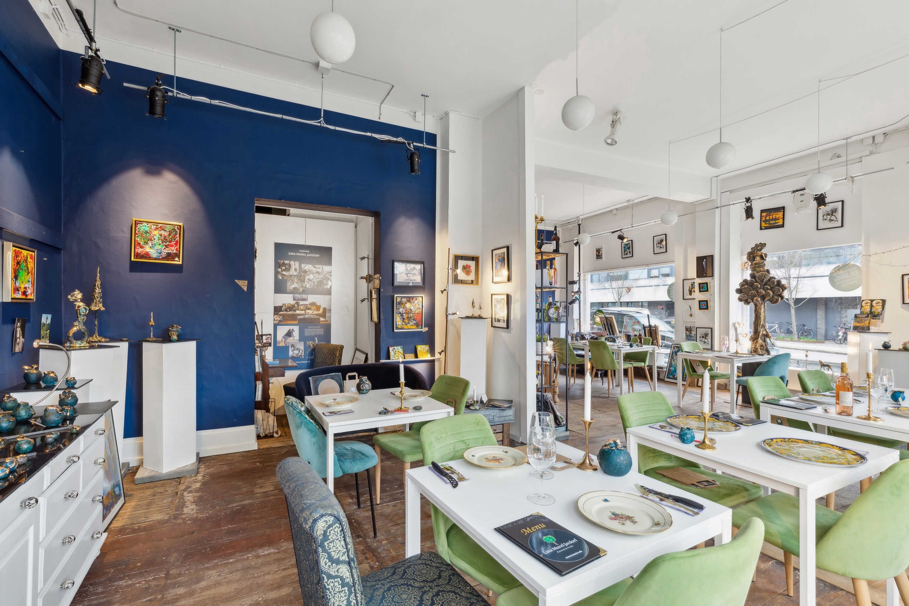 En moderne møbelforretning med masser af kunstværker på væggene og hyggelige grønne stole omkring hvide borde