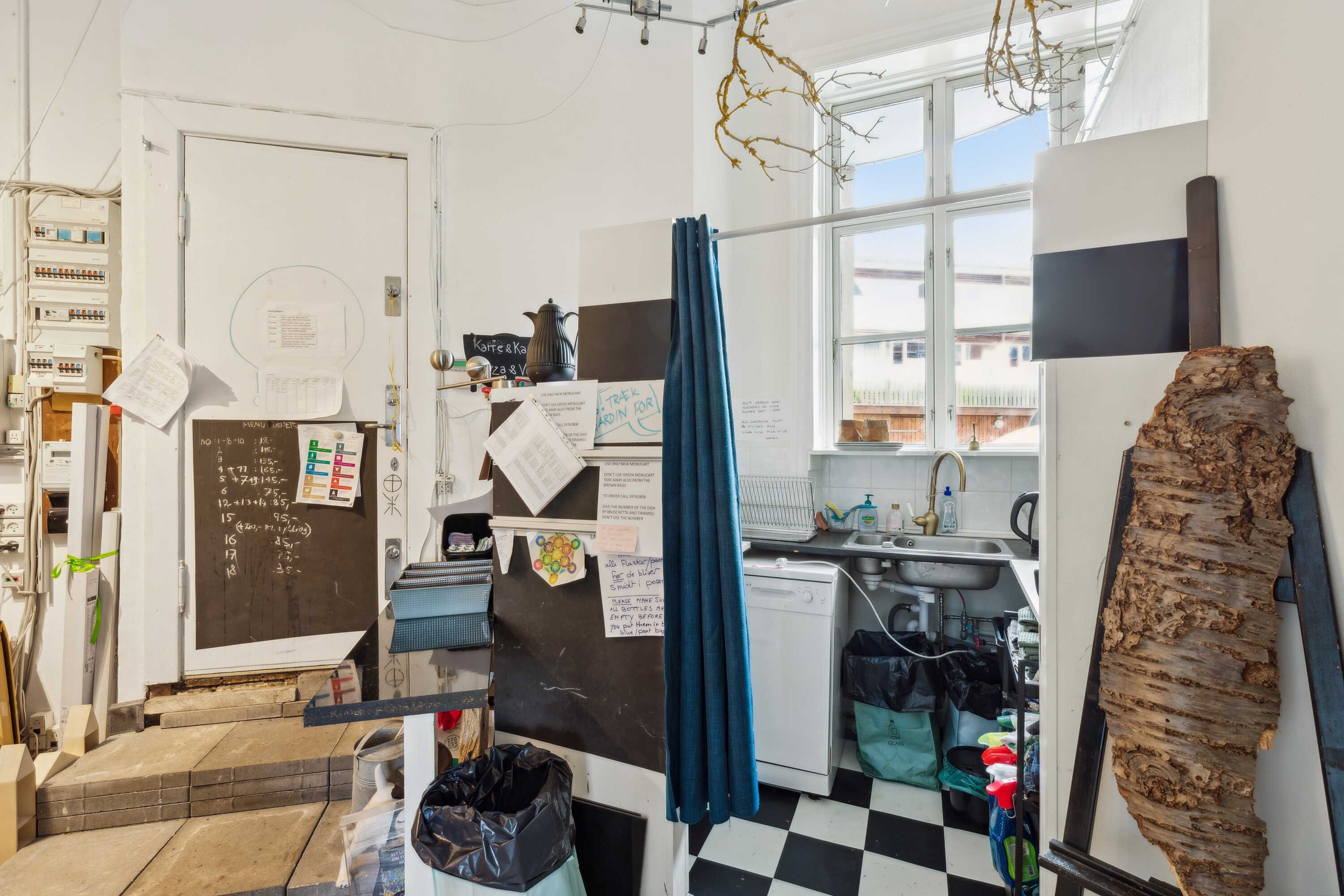 Lejlighed med loftsværelser og lyse lofter, fuld af genstande og noter på væggen. En stor skrivebord med en høj stol og en