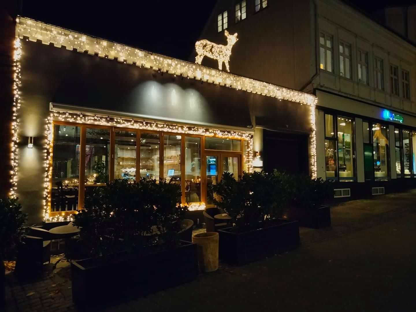 Restaurant med julepynt, krans og julepynt med dyreskilt på taget og lys i vinduet og på gaden