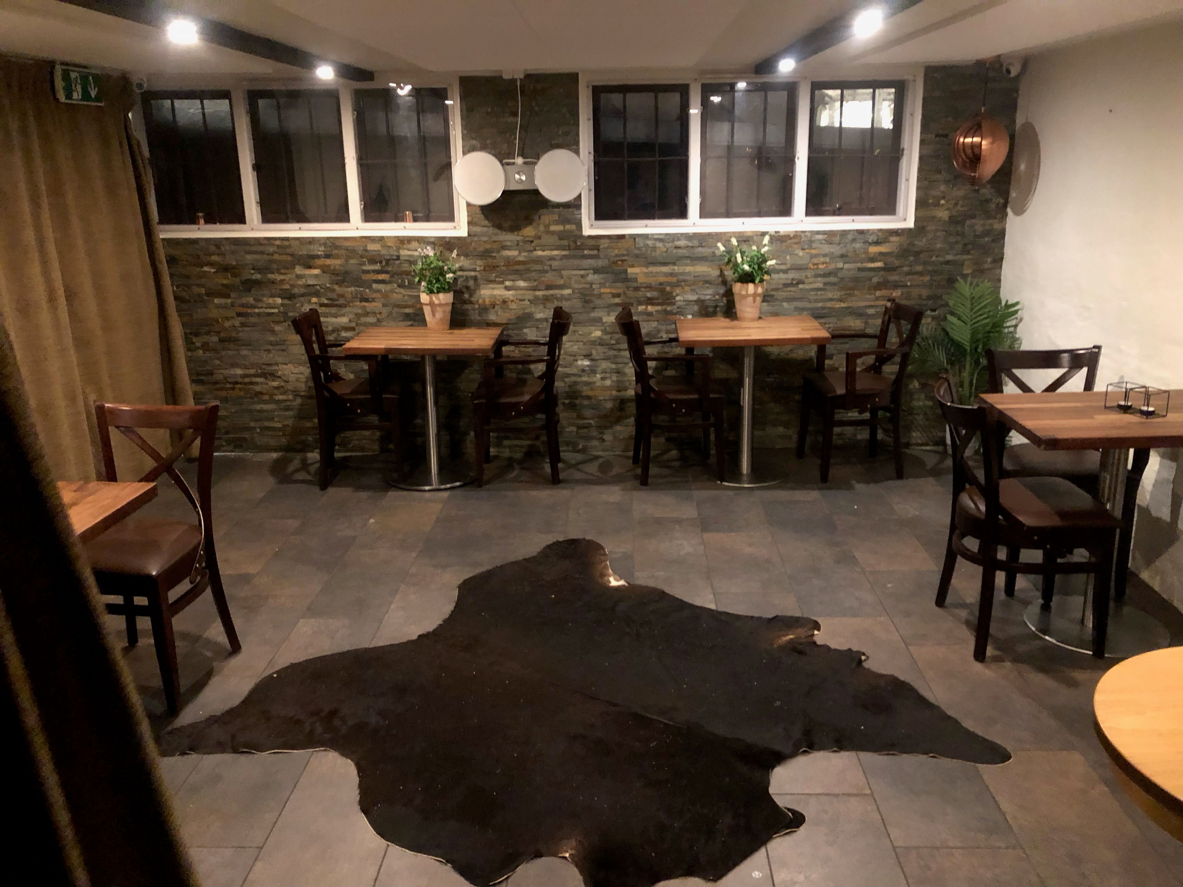 Moderne restaurant med fire to-persons borde, lyse lamper og en stor brun pels på gulvet.