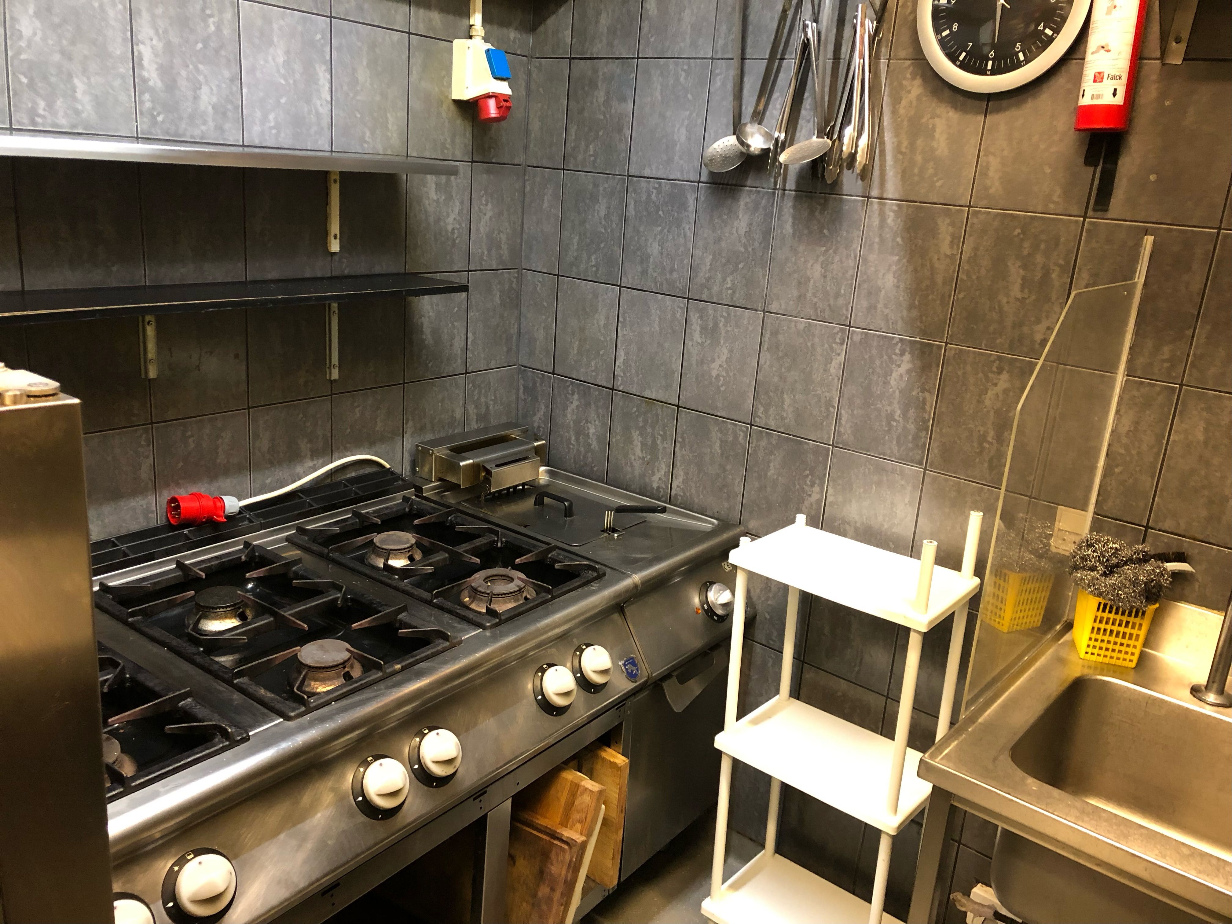 Gaskomfur med fire brænder og et ekstraktorventilator på væggen med en brændsletæller og køkkenredskaber