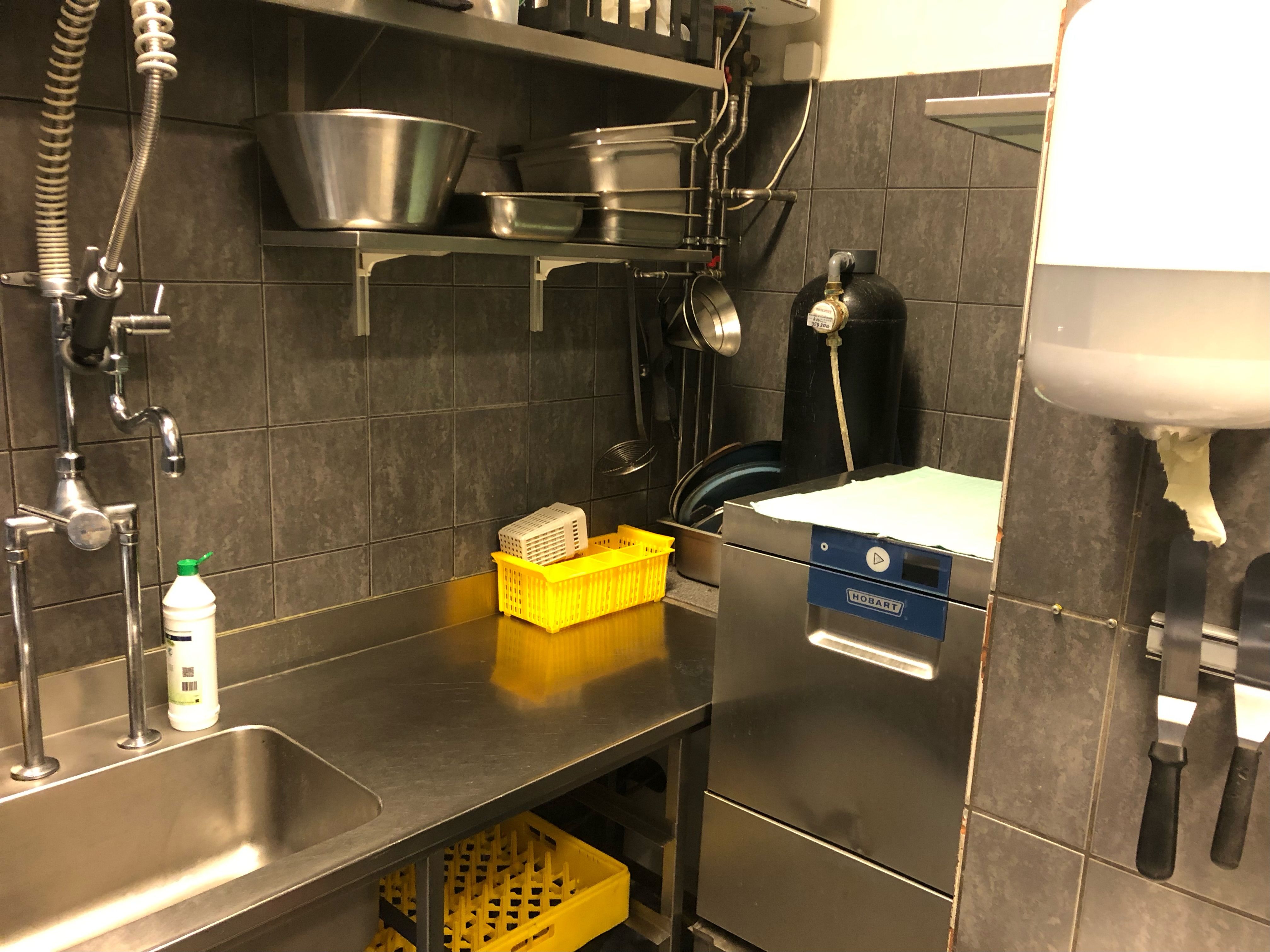 En ren og velorganiseret kommerciel køkken med flere rustfri stålapparater og en stor kasse med plast.