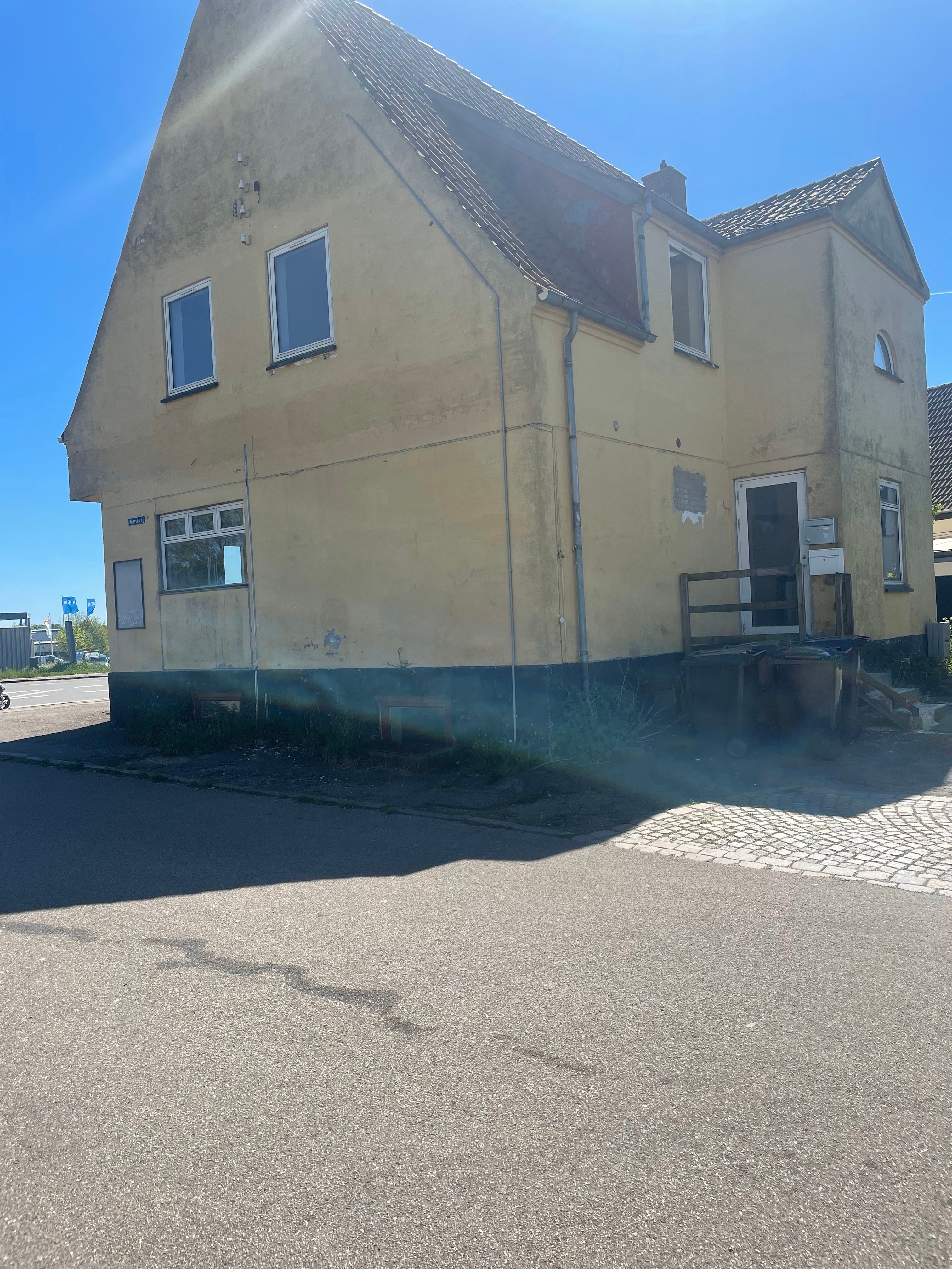 En gammel gul bygning med fire vinduer og en indgang, der er lukket med en dør og et stålrammer.