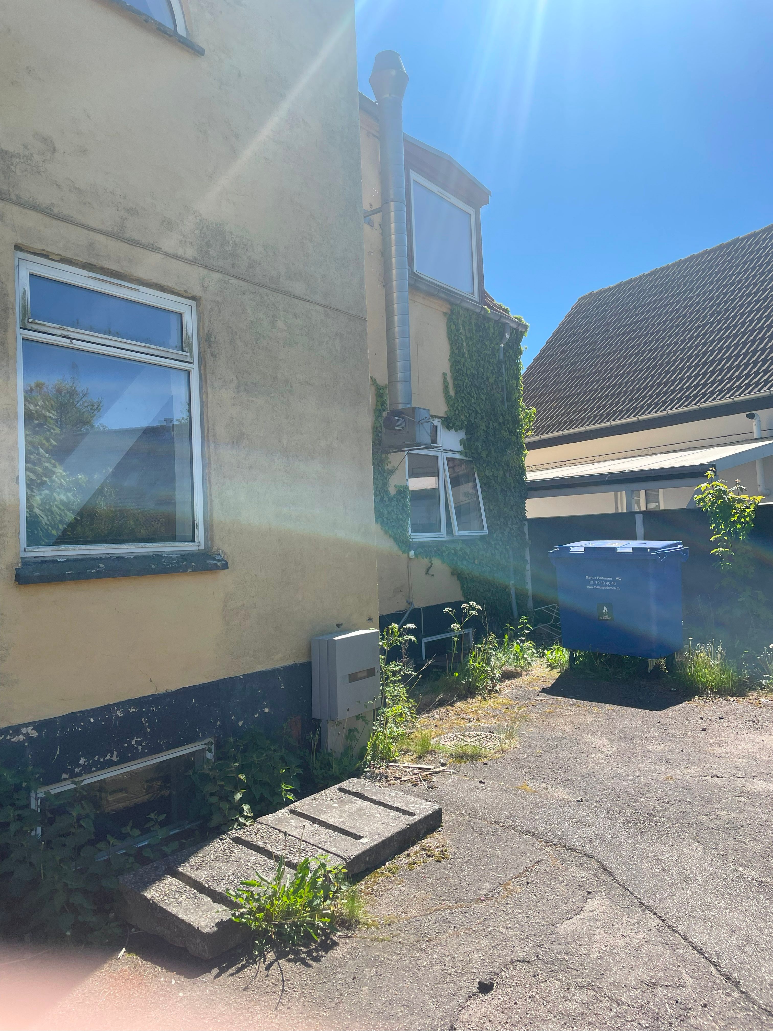 En gård med en vinduesramme og en lille trappe foran en mur og en kassevogn med en tekst på dens side