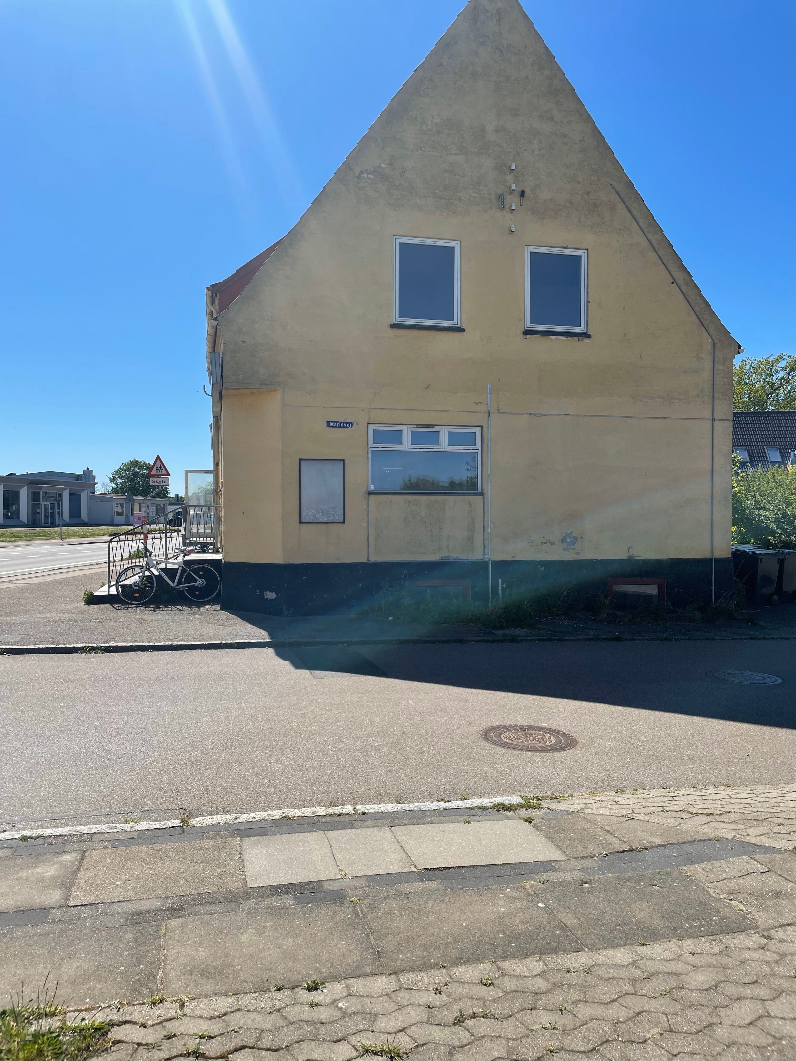 En gammel, gul bygning med tre vinduer og en dør på Gl. Ringsted. En cykel står parkeret ved trappen og et skilt står bagved