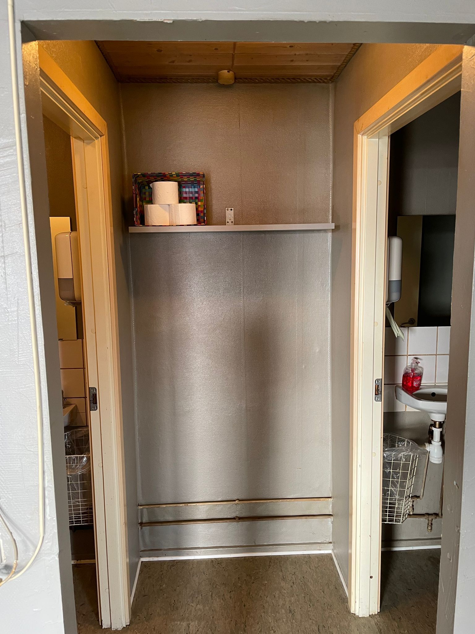 Toiletrum med to toiletpapirruller på hylde og håndsæbe ved håndvask