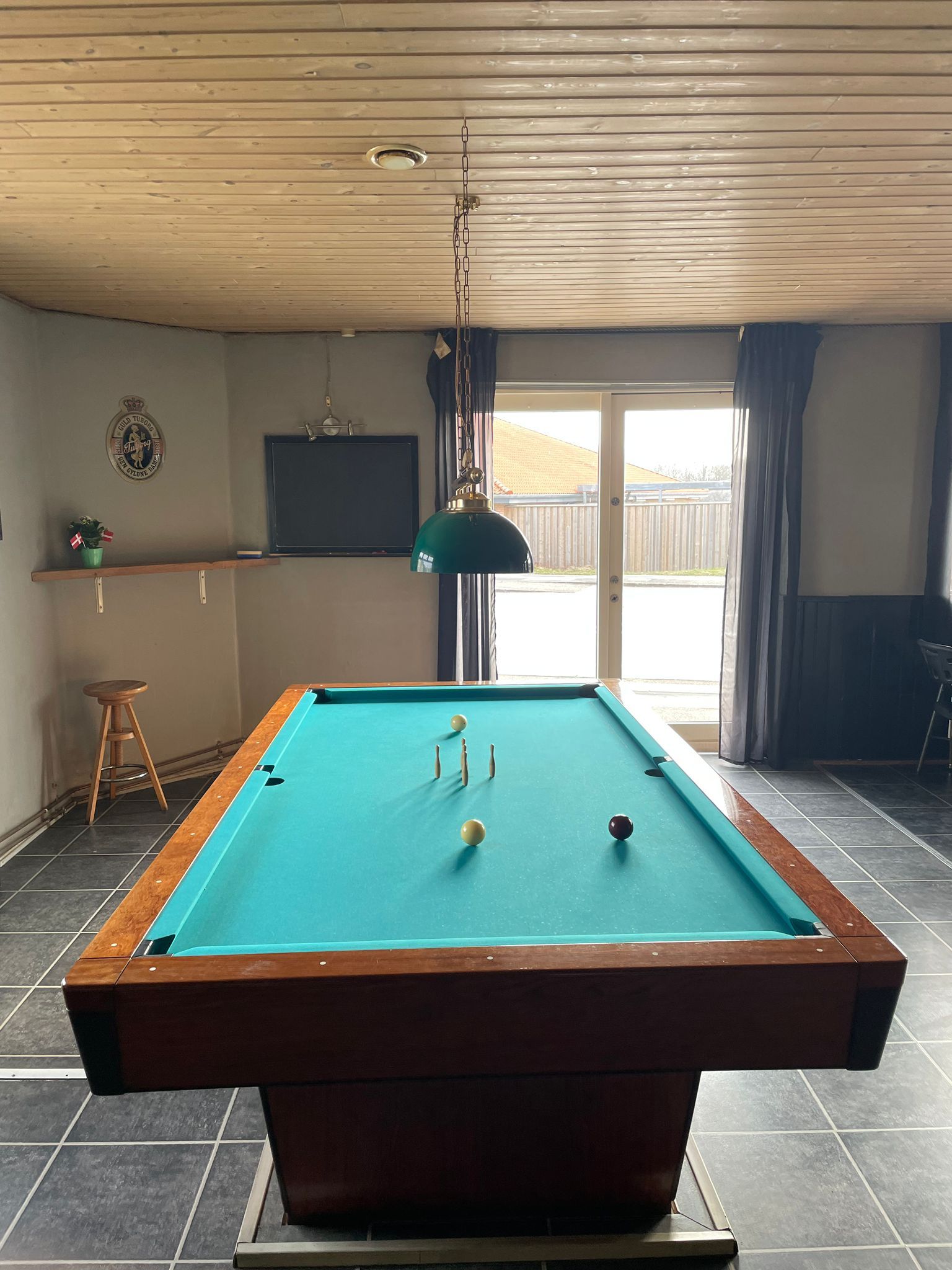 Billardbord i poolrum med tegnet gul bold og fire hvide bolde, samt en kælenavnsskilt på væggen