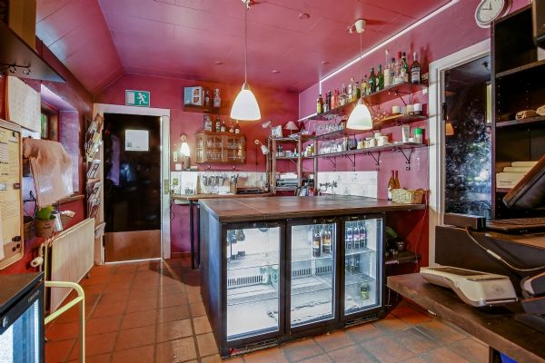 Vinkøleskab med glasdøre i kro med en lysekron og hylder med flasker og glas i en lille stue