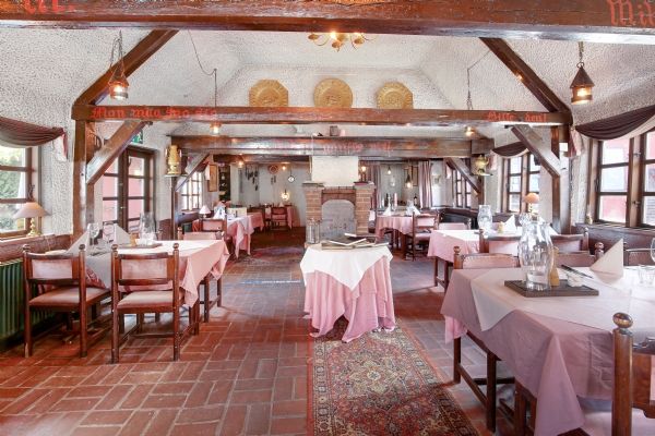 Pinktabelkledet restaurant med røde murstengulve, højt loft med brædder, smukt lysarmatur og lyseruder med gardiner