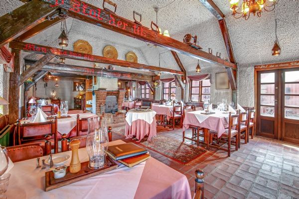 Klassisk kro med forgyldte bjælker, lyserøde bordkluder, krystallysekroner og en pejs i enden af værelset