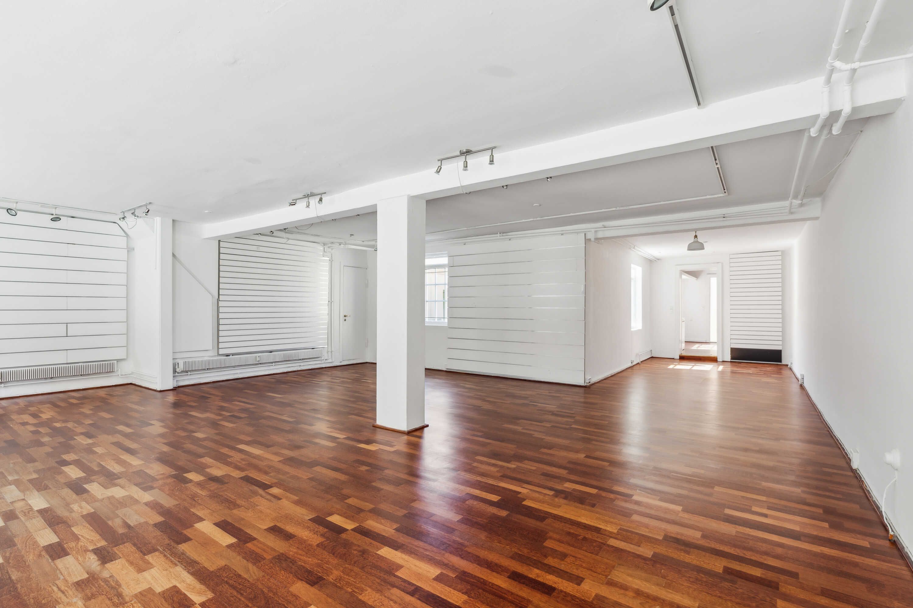 Lejlighed med lyse gulve og vægge samt flere hvide skurvægge. To hvide søjler står midt i rummet og forskellige lys på loftet