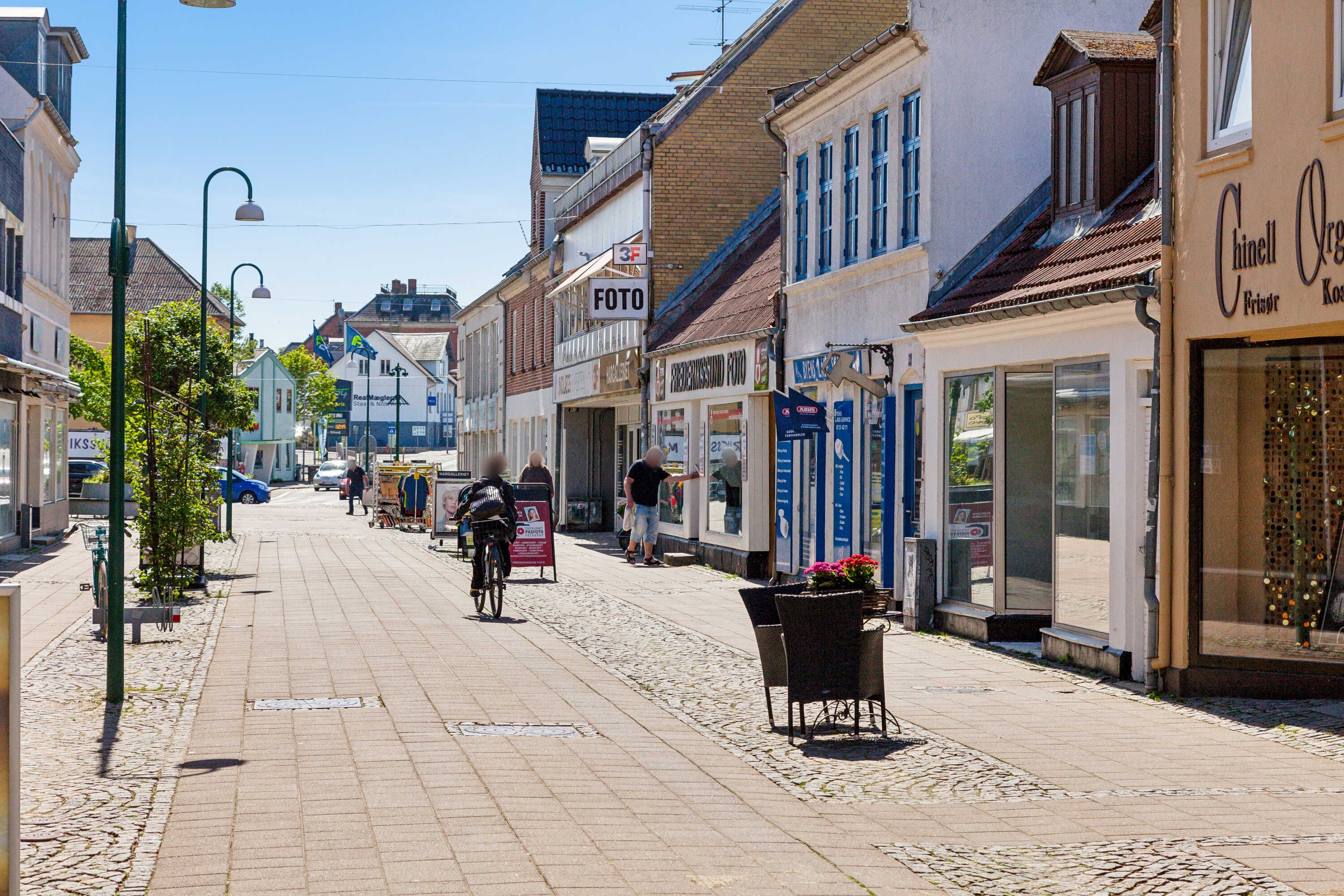 Foto og forretningslokaler ligger langs en hovedgade med cykelrytter og forbipasserende mennesker