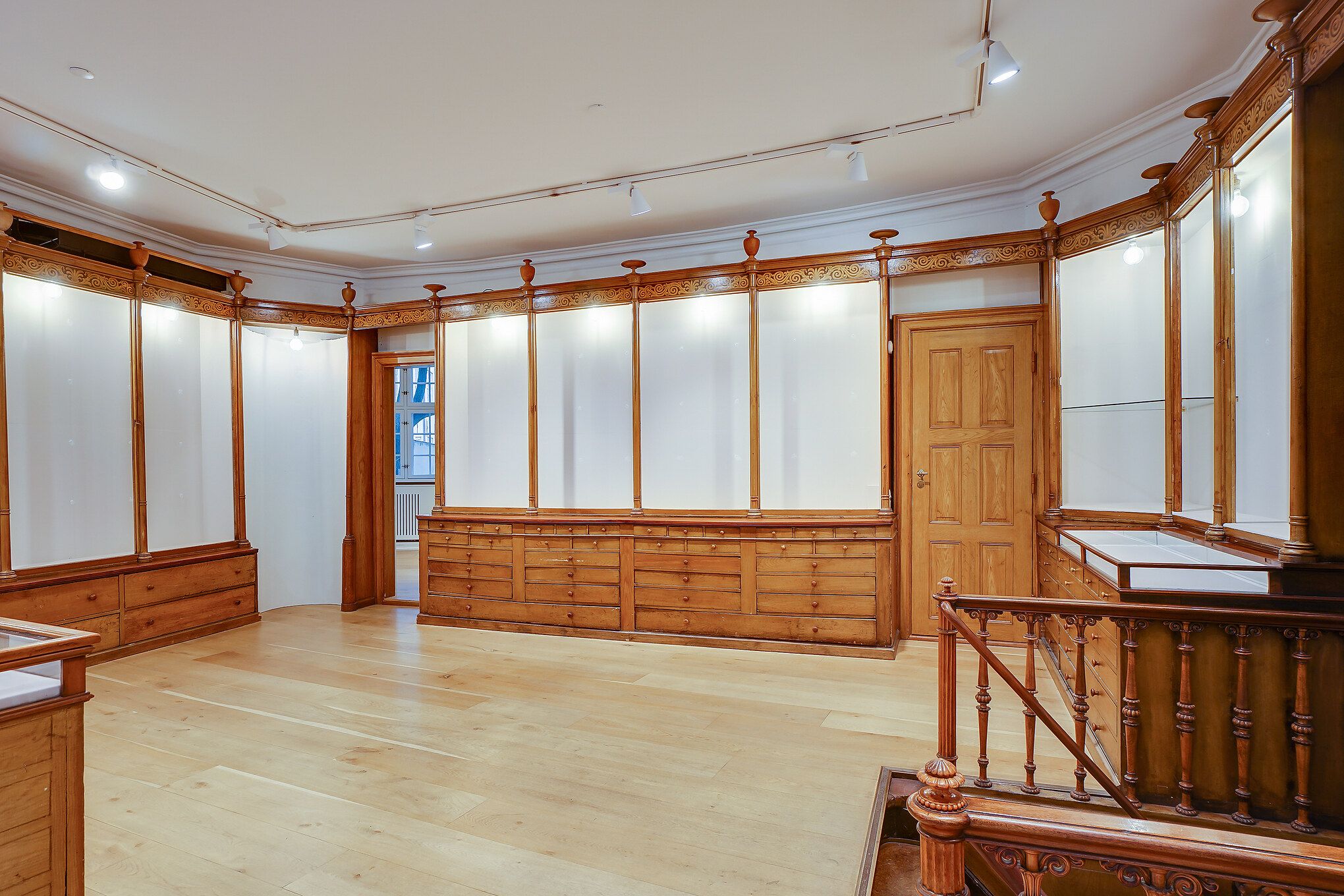 Elegant værelse med lysegul gulv og træskabe, højt loft med hvide vægge, lysekroner og to træhåndtag på højre side