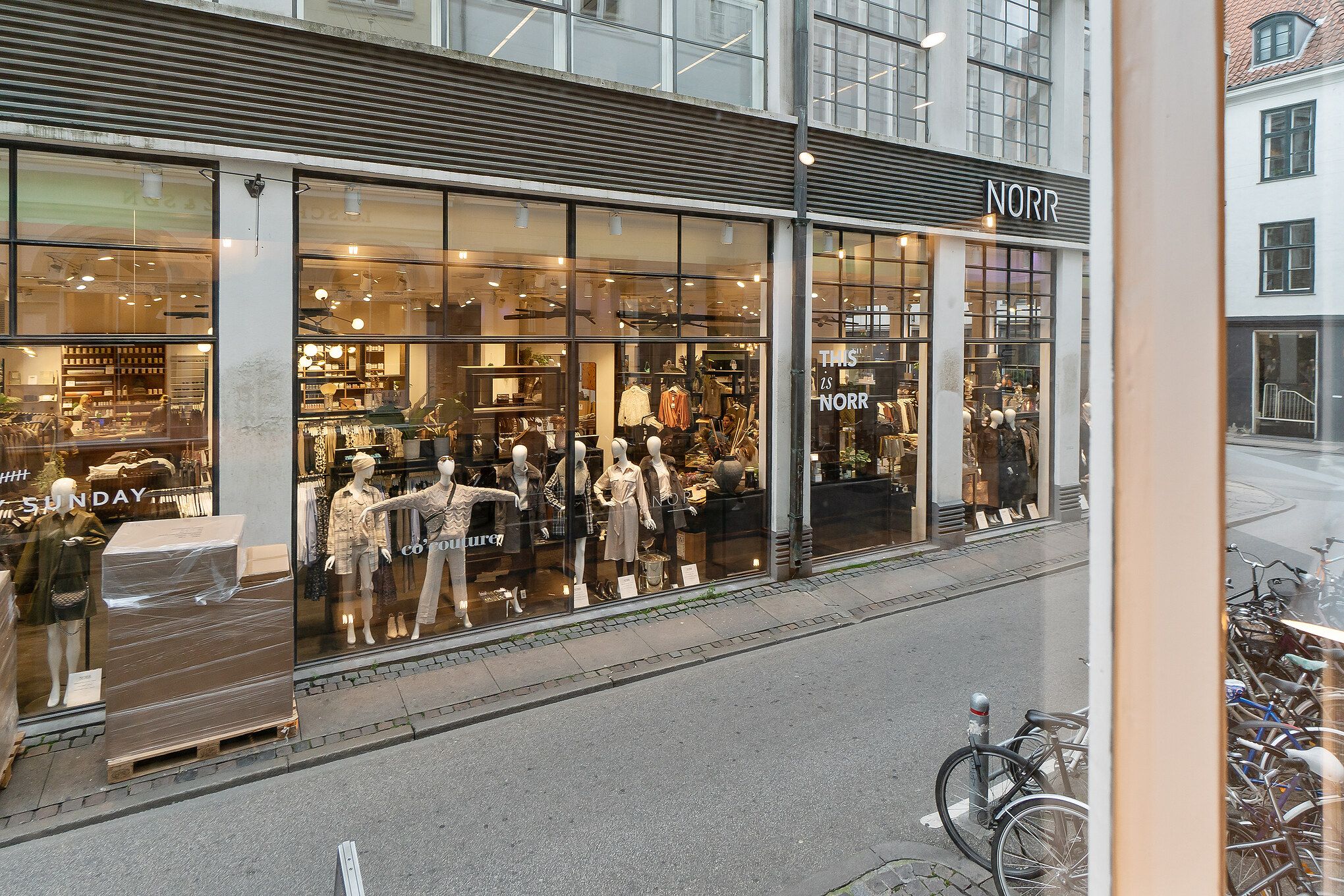 Alttekst: Nord-butik på Tscherningsgade med tøj i vinduet, og mange cykler parkeret udenfor