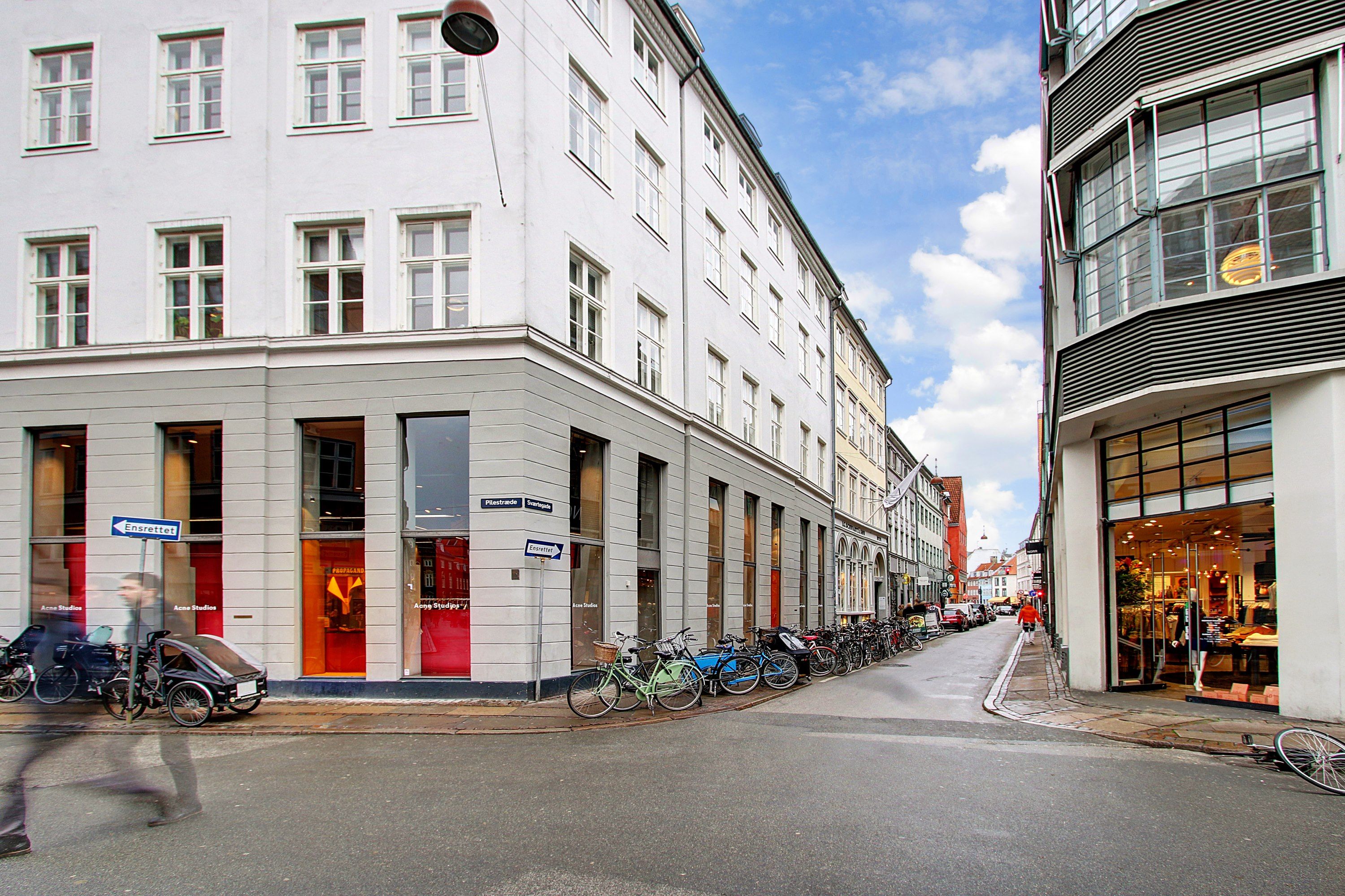 Mennesker går på gågaden med cykler parkeret langs gaden, hvor der er butikker og huse med mange vinduer