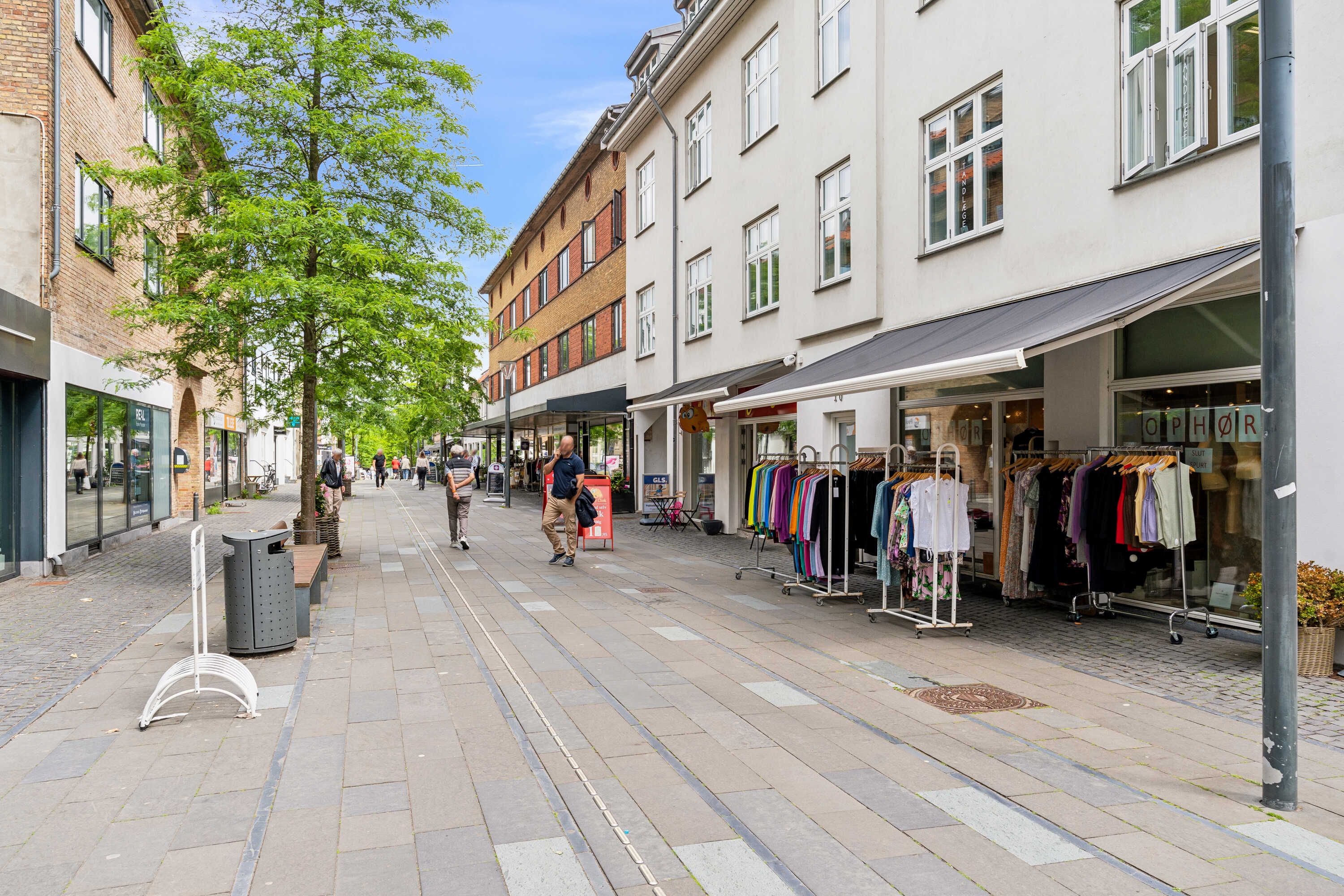 Et søjlegang med søjler, træer og butikker med tøj i udsigten, og mennesker går rundt i en by