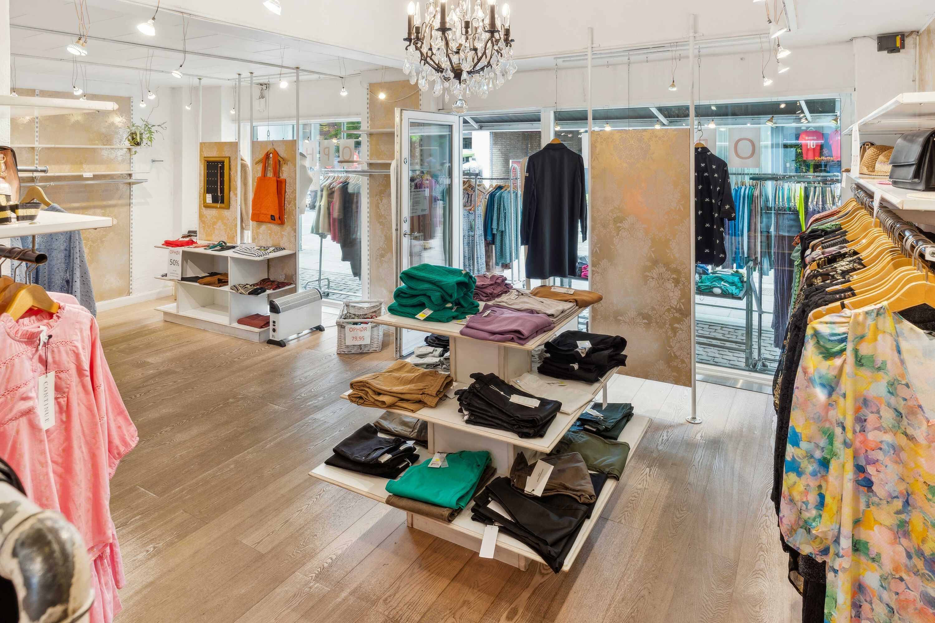 Lys, rummelig butik med klædeskab, hylder med sort og grøn tøj, og tøjvægge i hjertet af Hørsholm