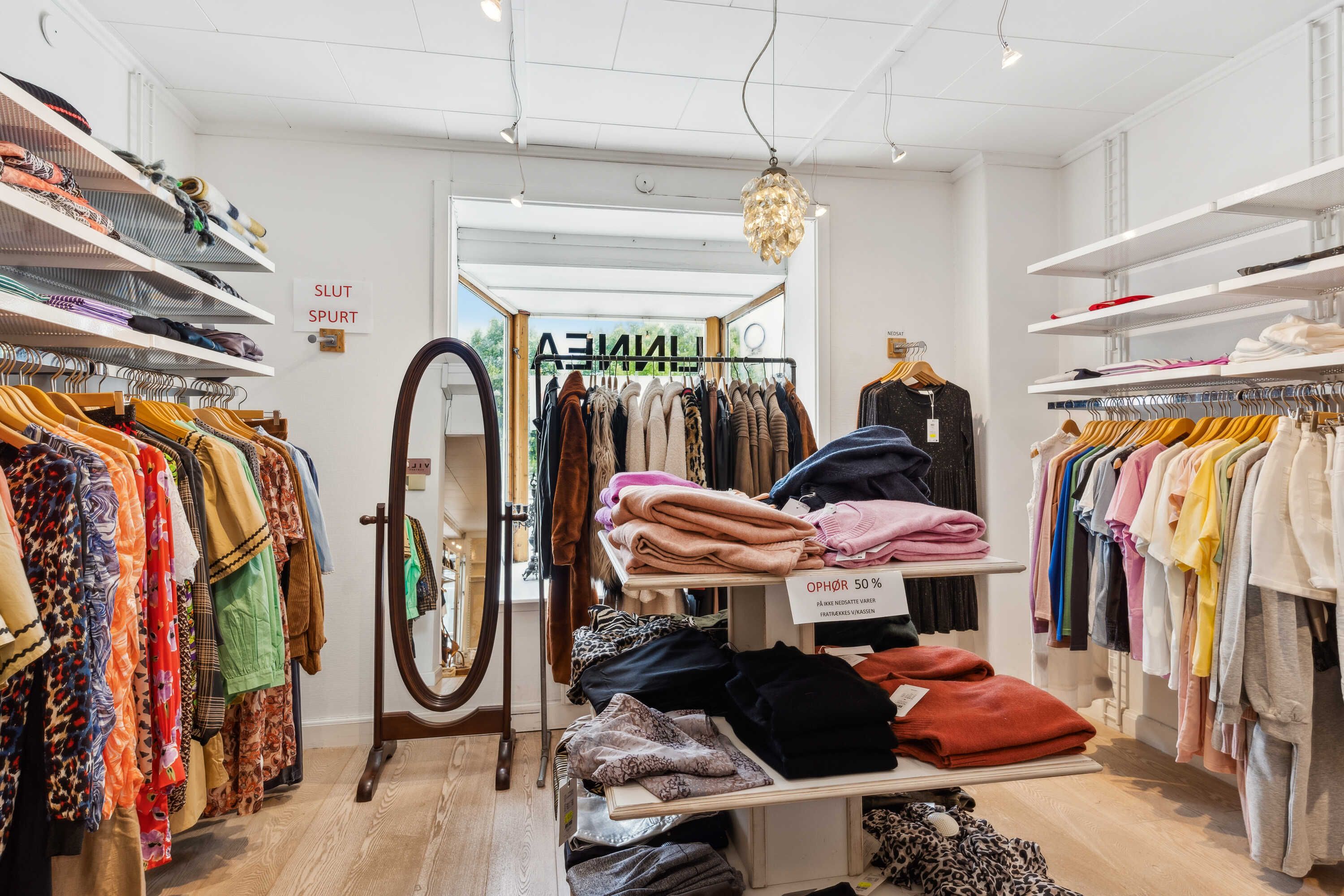 Butik med tøj i forskellige farver og størrelser, hængende på hængere og stående på hylder og stativer