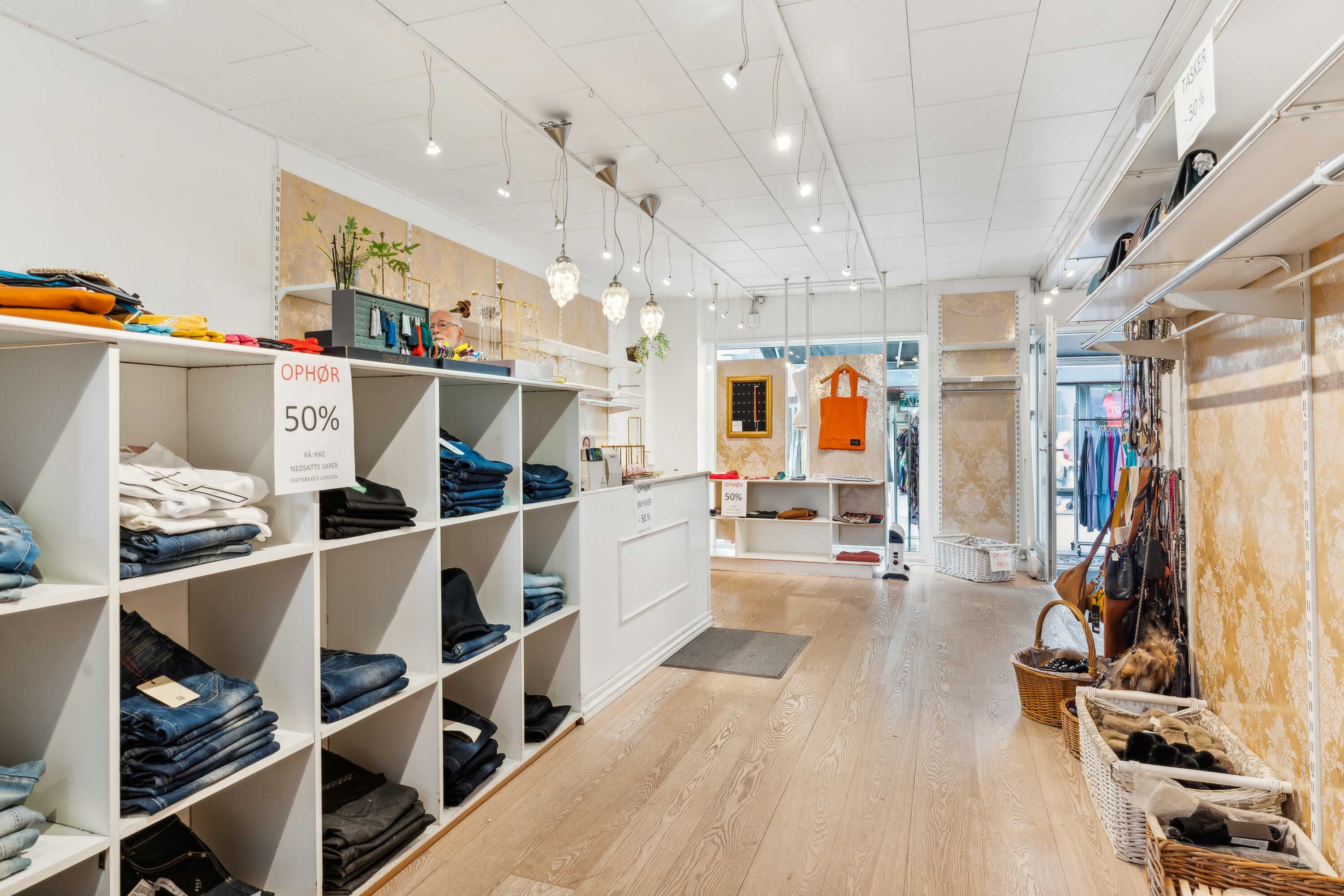 Foto af en nyindrettet butik med tøj og sko på hylder, trægulve og lyskroner. Butikken har 50% rabat.
