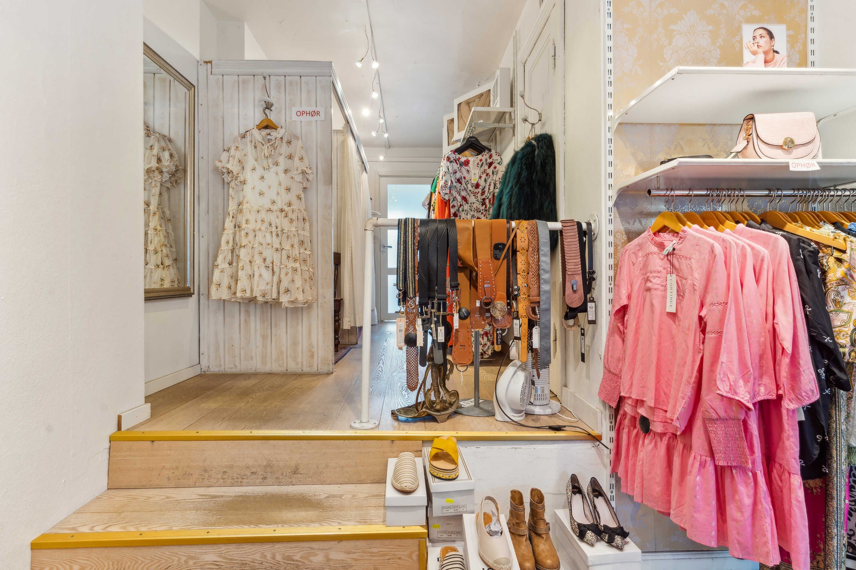 Kvinders tøj og sko er udstillet i et butikslokale med hylder og stang til hængeklæder