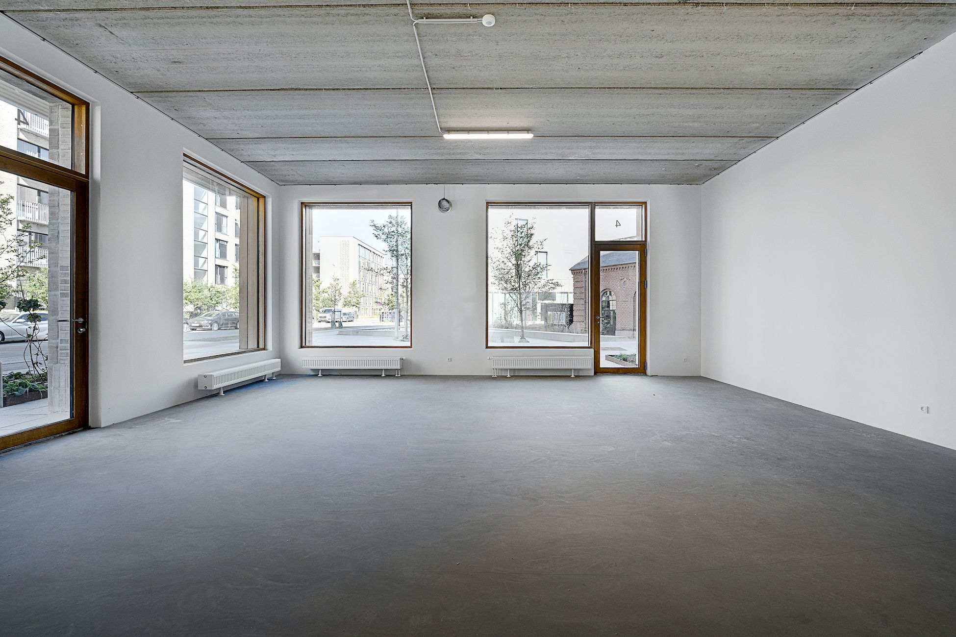 Et tomt rum med hvide vægge og gulv, tre store vinduer og lysekroner og radiatorer på væggene